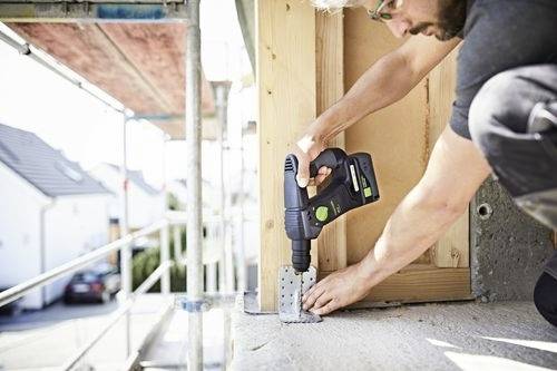 A person uses a power drill to secure a metal bracket to a wooden structure, suggesting construction or renovation work in progress.