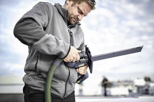 A person uses a saw outdoors, focusing intently, wearing a gray jacket. The sky is cloudy, suggesting a brisk day.
