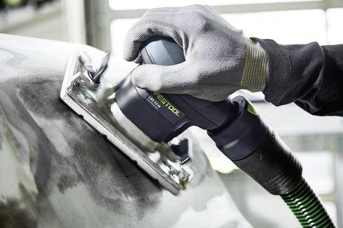 A gloved hand uses a power sander on a metal surface, smoothing the texture. The tool is connected to a green and black hose.