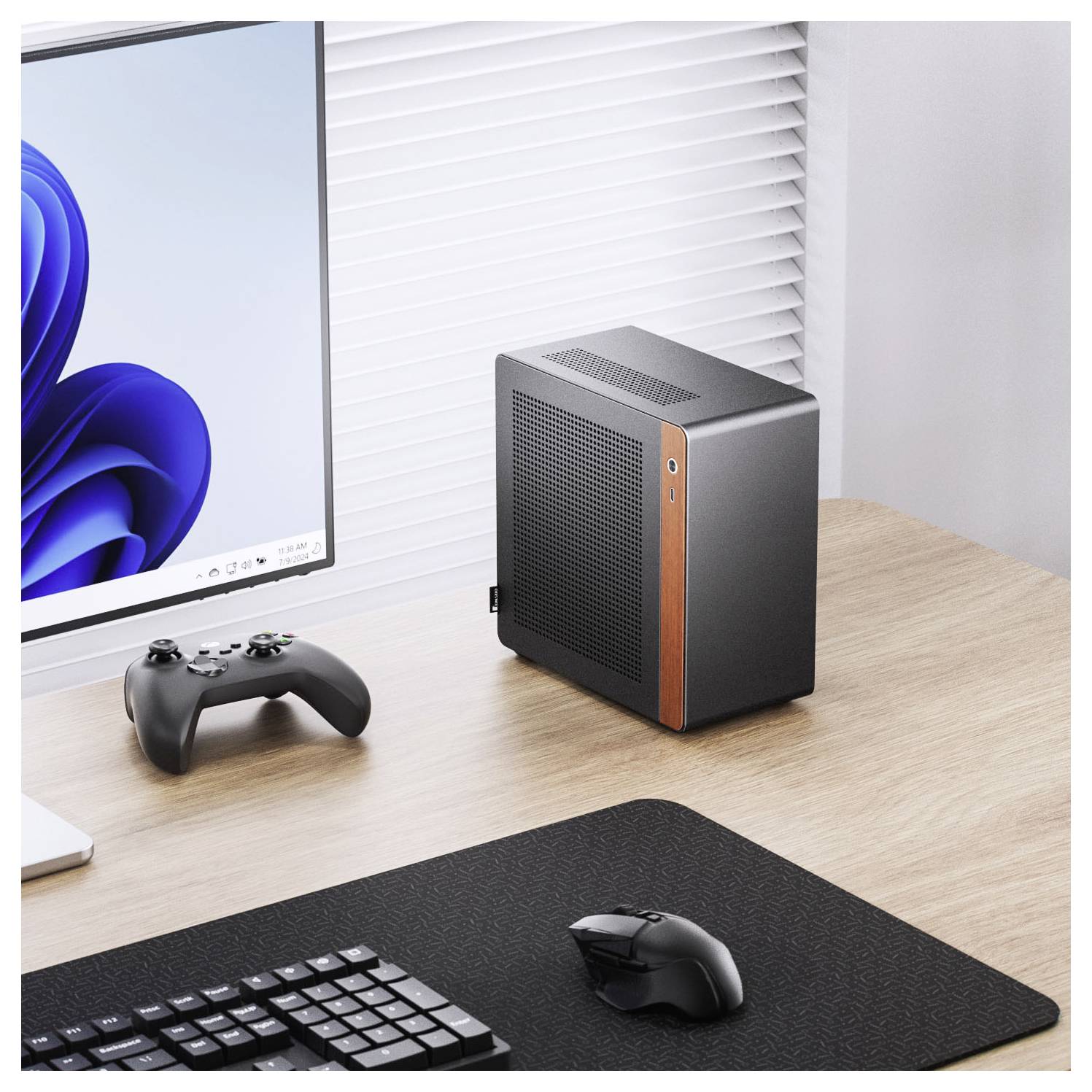 A sleek computer setup with a monitor displaying a blue geometric swirl design, a wireless game controller, a keyboard, and a compact, modern desktop computer.