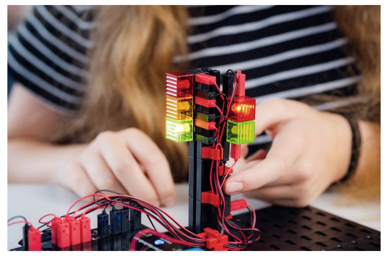 A person is building a small electronic project featuring a traffic light model with red, yellow, and green lights on a circuit board.
