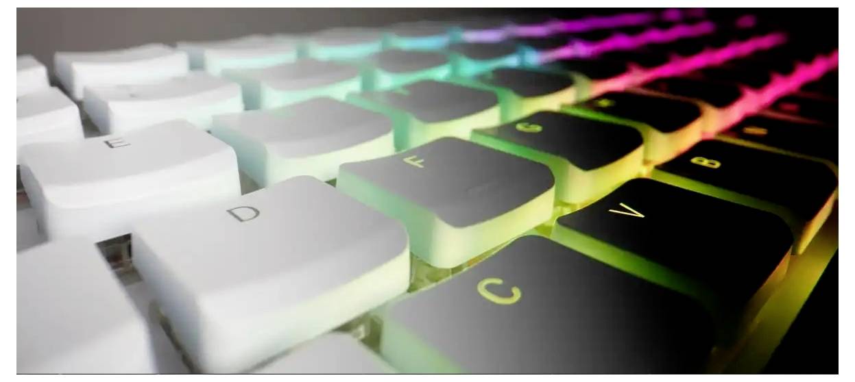 A close-up of a keyboard with white keys illuminated by colorful LED lights, transitioning from green to pink diagonally across the keys.