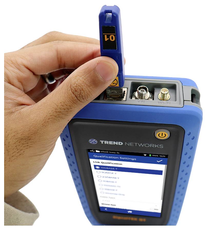 A hand inserts a network cable into a blue device displaying 'Link Qualification' on the screen, with several connection ports visible.