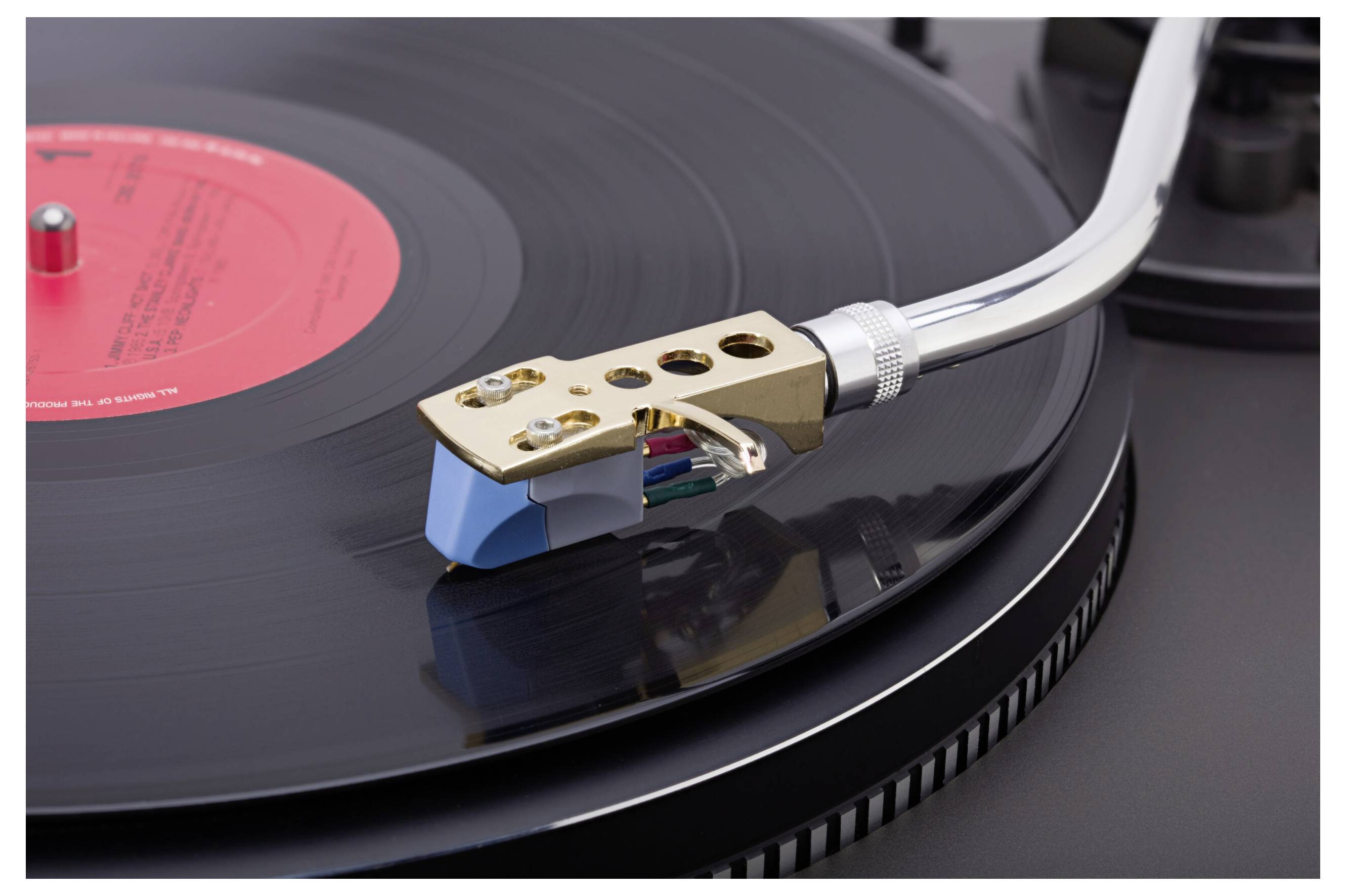 A close-up of a vinyl record player with a spinning black record. The turntable's tonearm is lowered, and the needle is on the record.