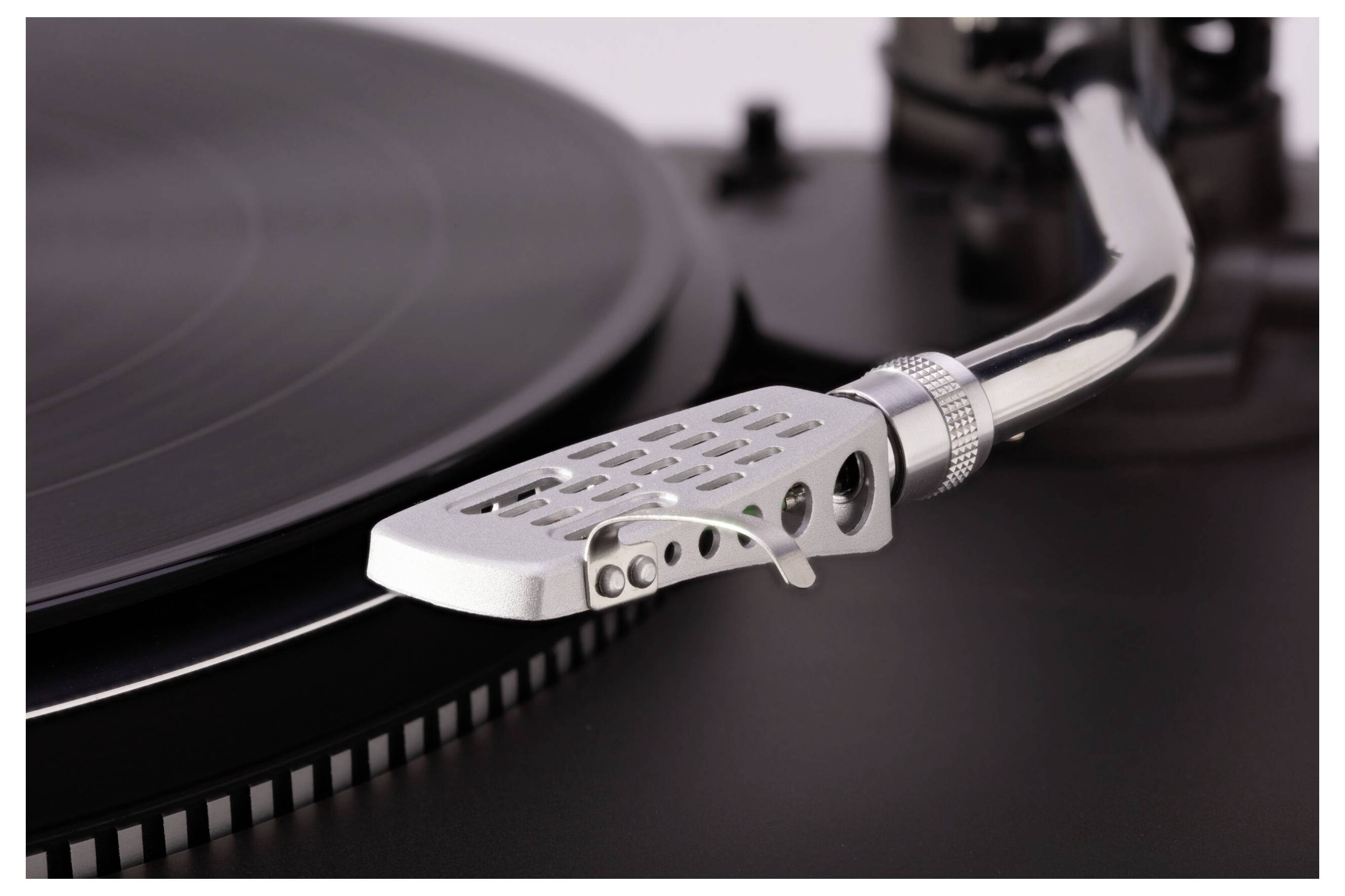 A close-up of a turntable's tonearm and stylus positioned over a spinning black vinyl record, highlighting the grooves and metal details.