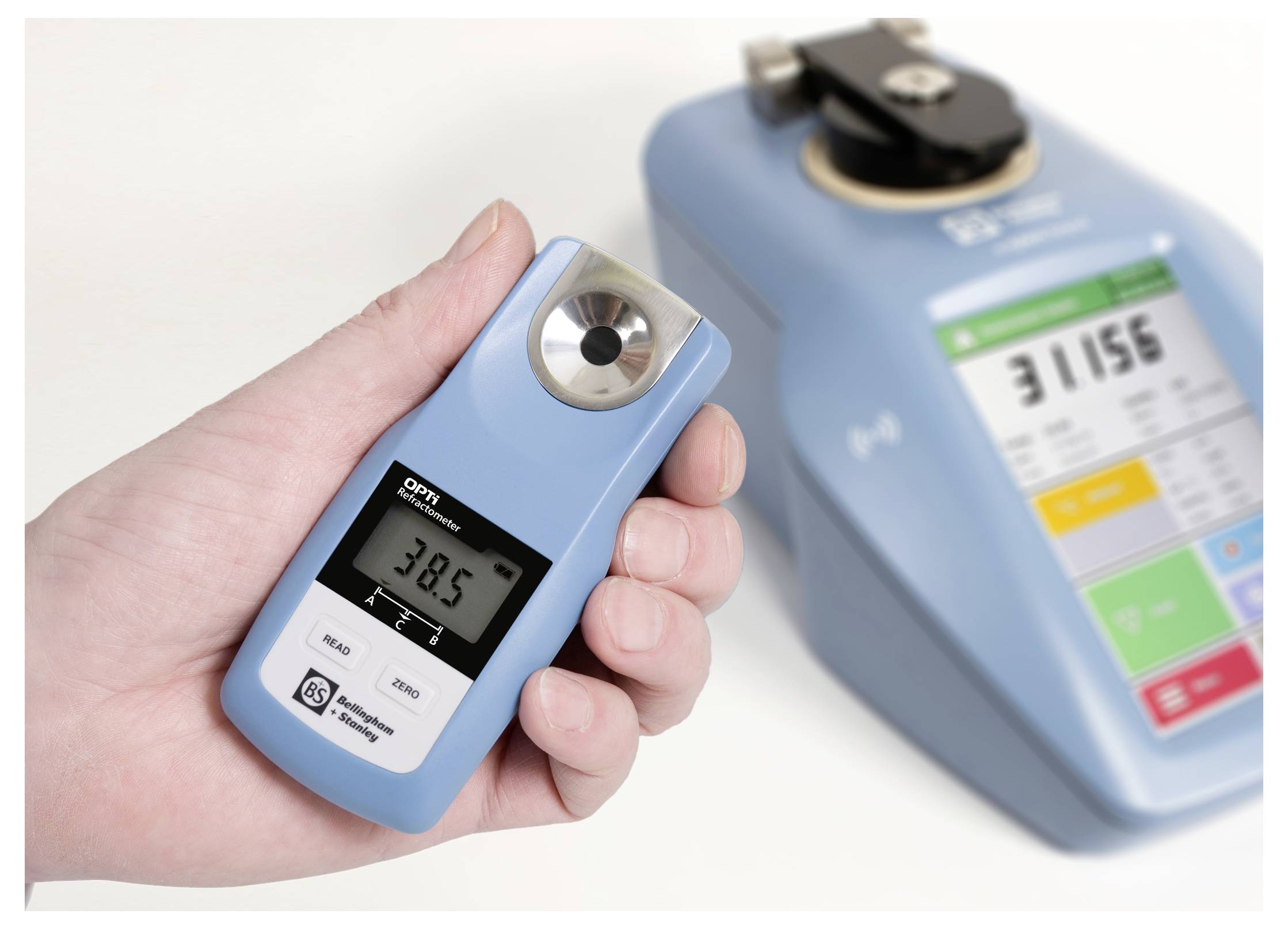 A hand holds a digital refractometer measuring '38.5'. A larger blue measuring device with a digital display is in the background.