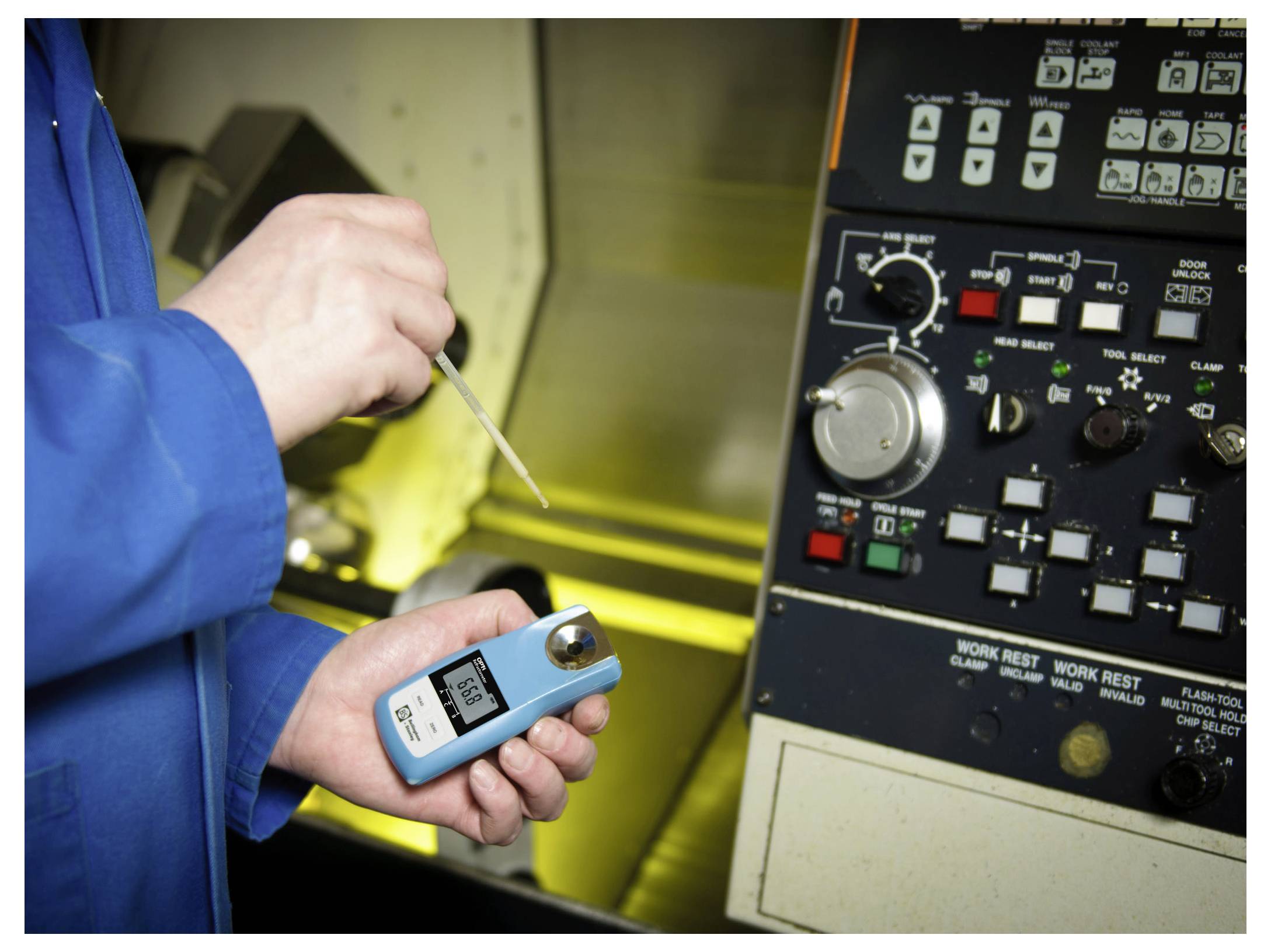 'A person in a blue coat holds a digital refractometer near machinery, measuring liquid concentration. The device's screen shows readings.'