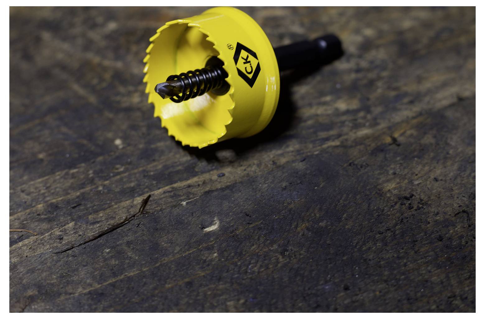 A yellow circular saw attachment with a metal spring center is placed on a textured, dark wooden surface.