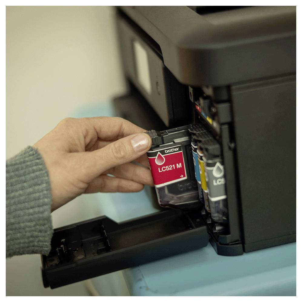 A hand is installing a red ink cartridge labeled 'LC521 M' into a printer, indicating maintenance or setup of the printer's ink system.