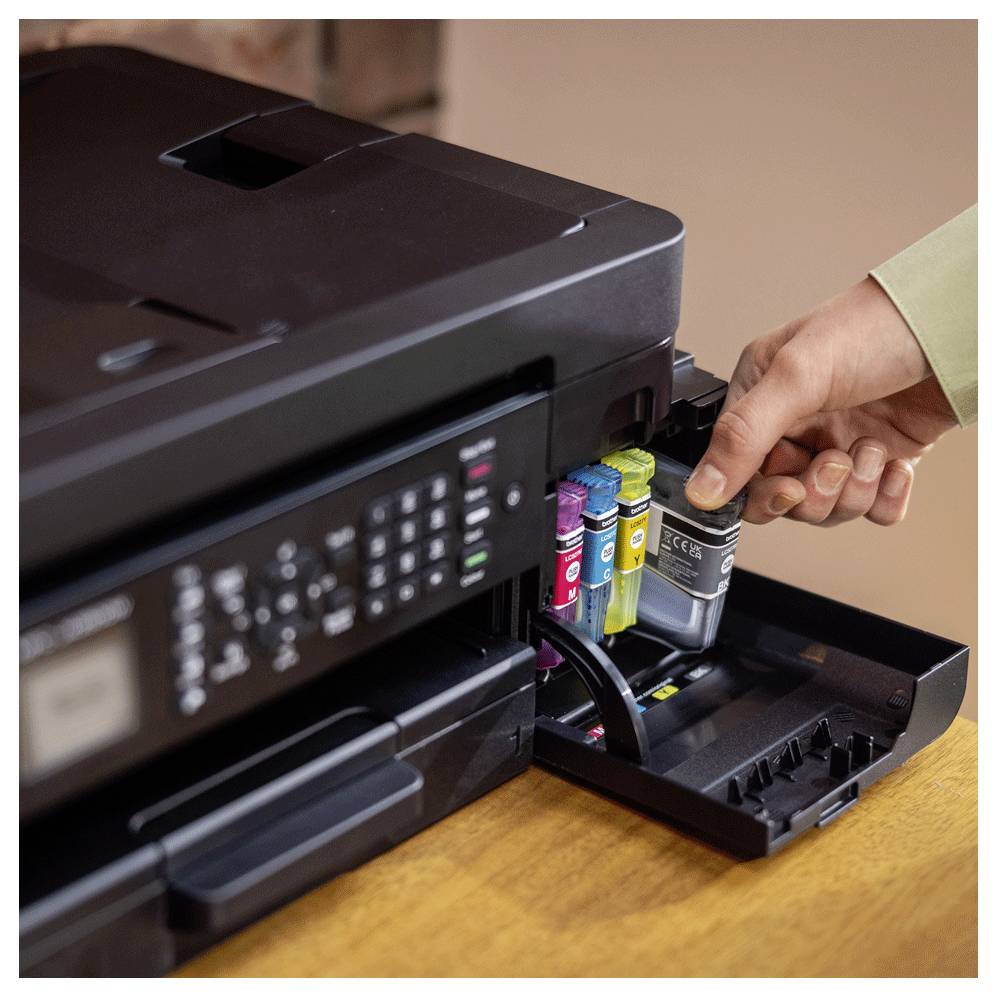 A person replaces a black ink cartridge in a color printer, with visible magenta, yellow, and cyan cartridges.