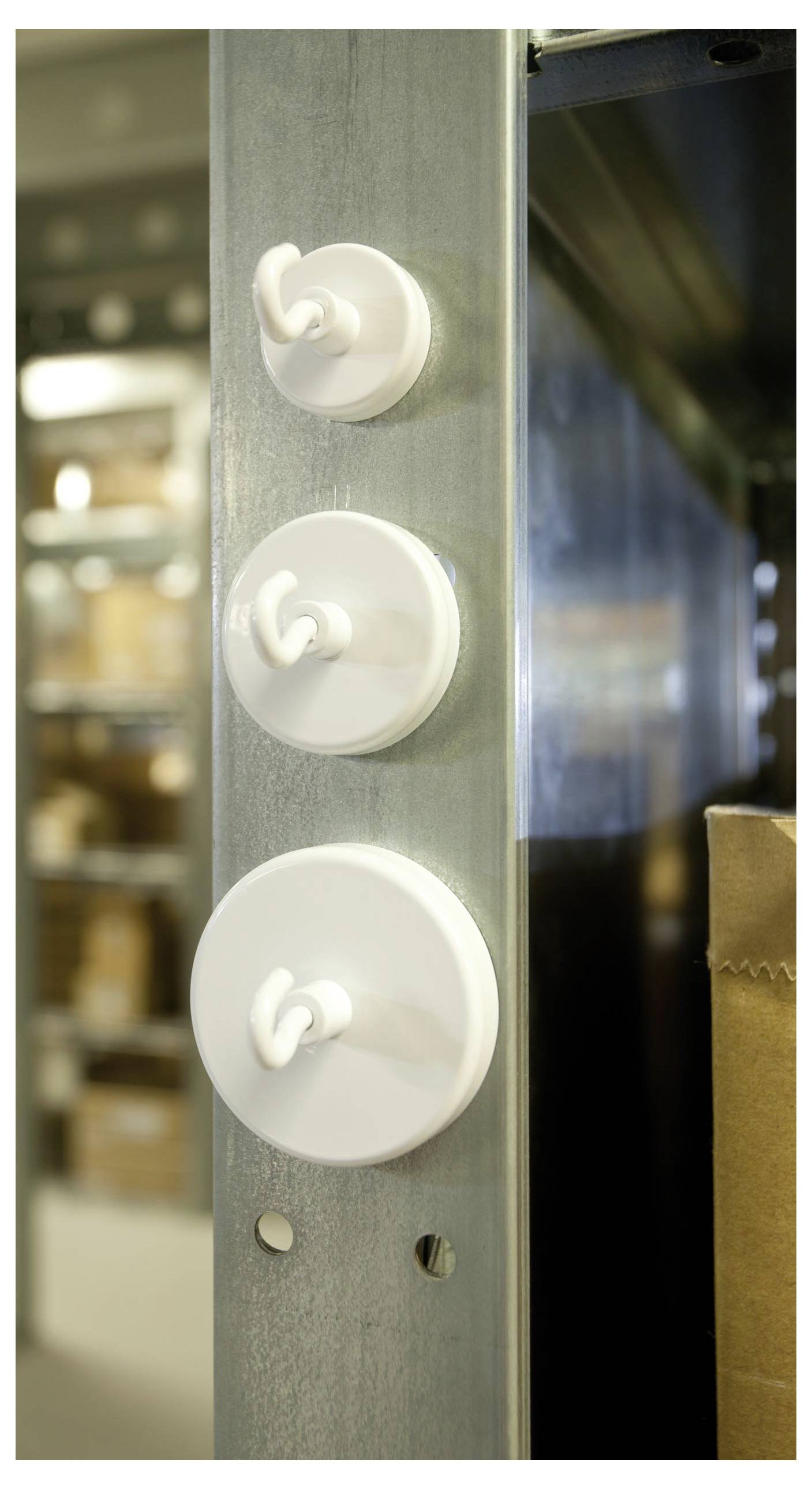 Three white hooks attached to a metallic shelf in a storage area, with shelves of boxes blurred in the background.