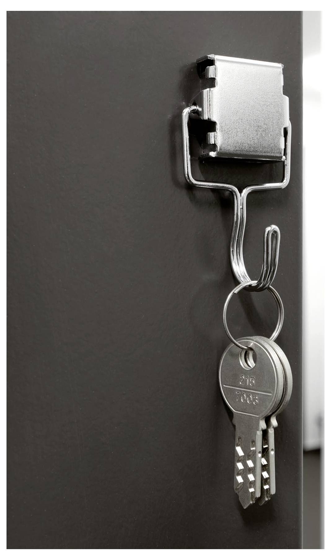 A set of metal keys hangs on a steel hook attached to a dark surface, suggesting secure storage or office use.