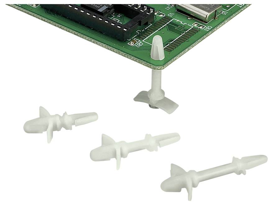 Plastic PCB mounting supports under a green circuit board, with three loose mounts lying nearby on a white surface.