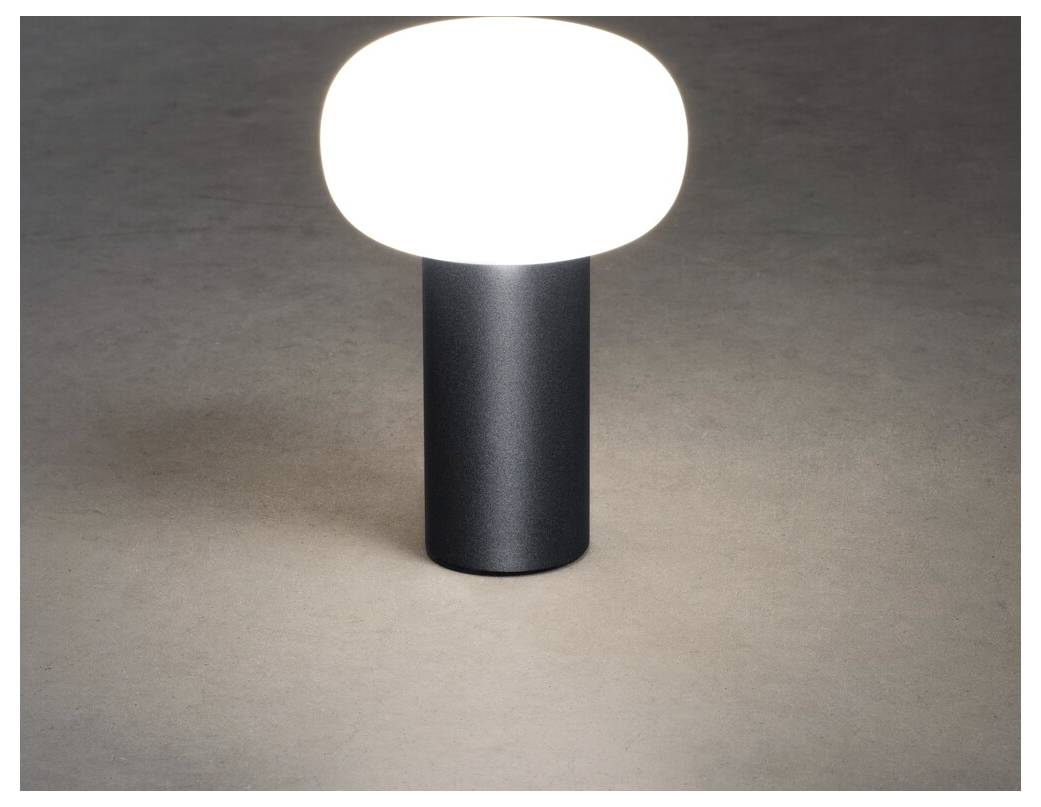 A modern table lamp with a rounded, white top emits a warm glow, sitting on a smooth, dark cylindrical base against a neutral background.