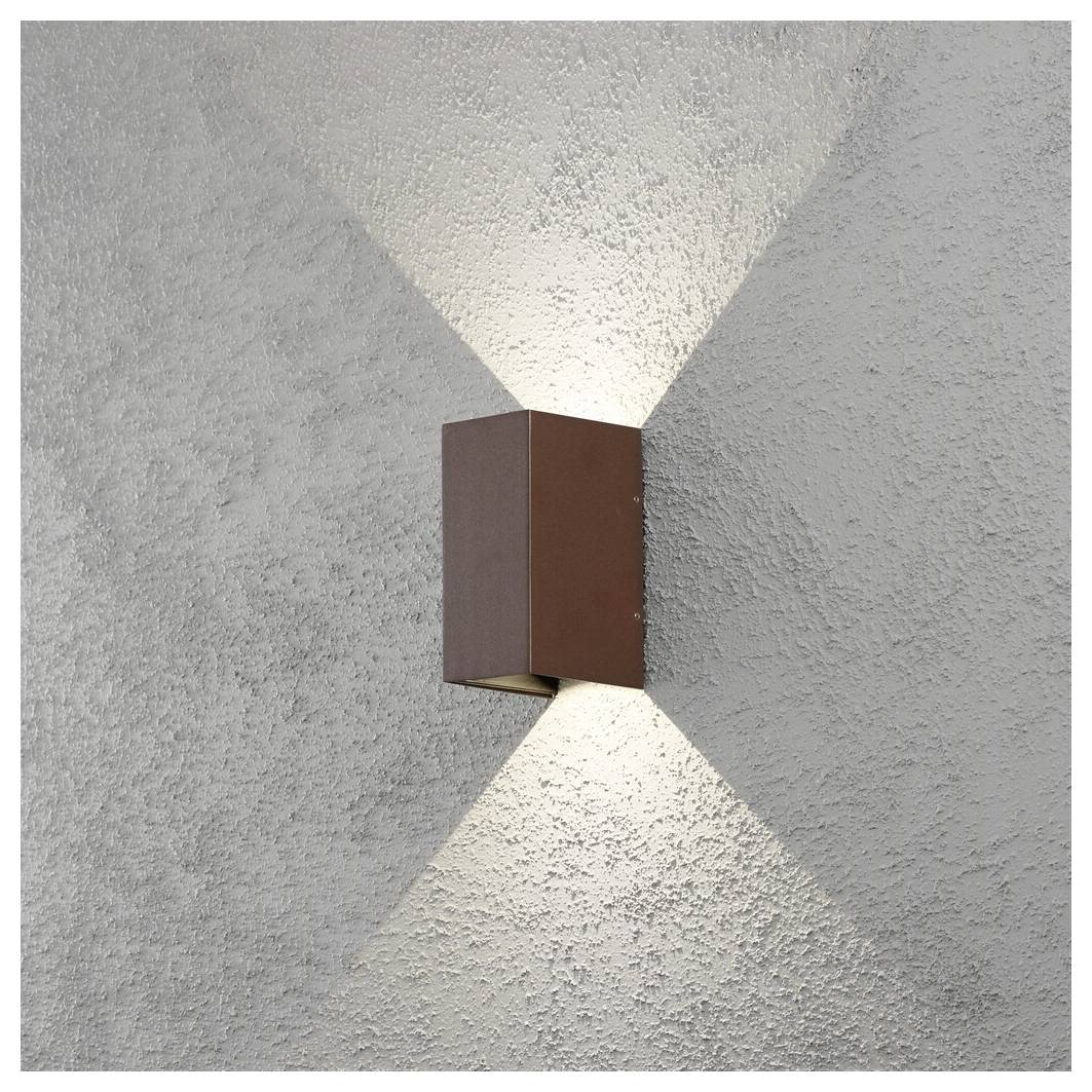 A wall-mounted light fixture casts two beams of light against a textured gray wall, one upward and one downward, creating a decorative effect.