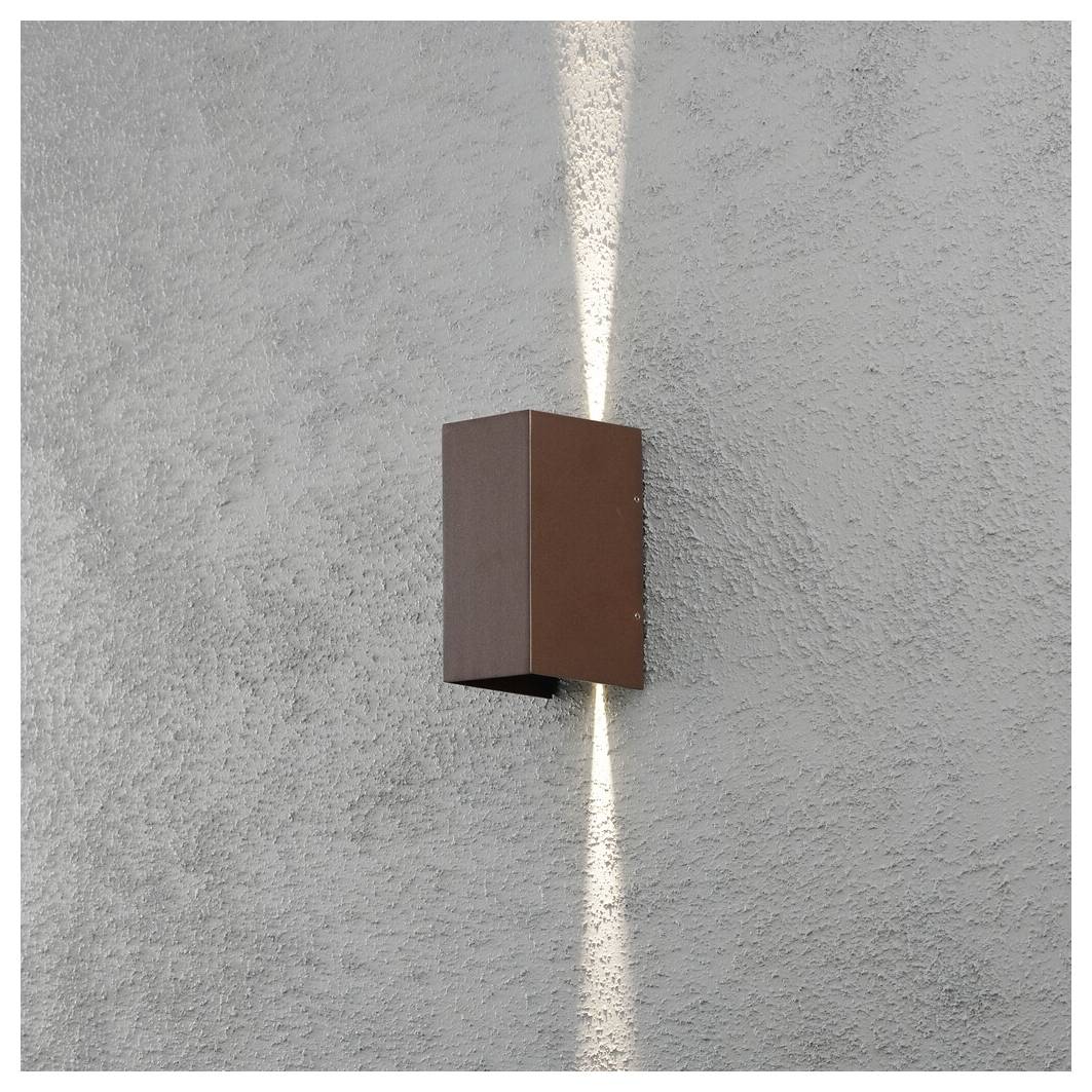 A modern, rectangular, brown outdoor wall light fixture mounted on a gray stucco wall, emitting vertical lighting above and below.