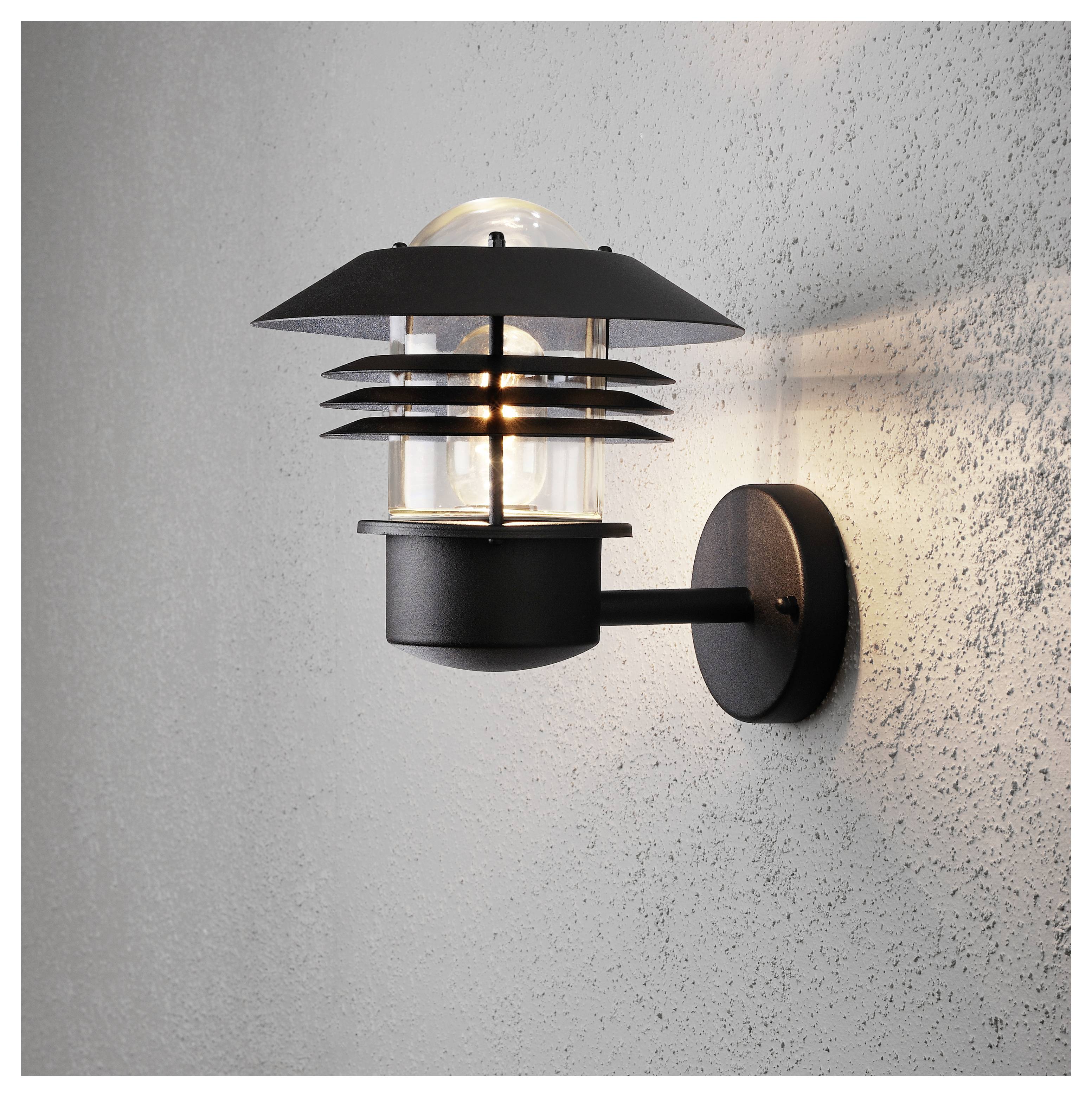 A modern black wall sconce with horizontal metal bars surrounding a clear glass bulb, emitting warm light onto a textured gray wall.