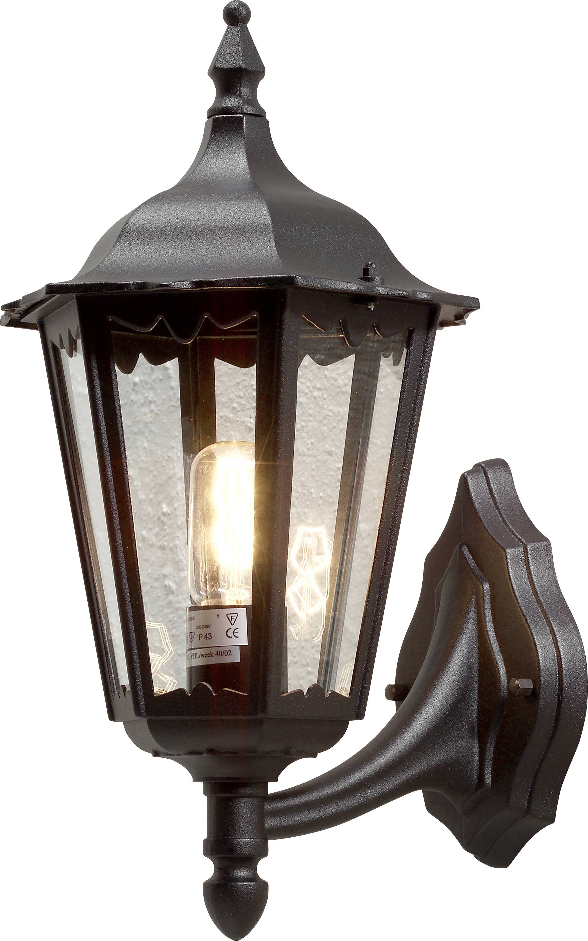 A black, vintage-style outdoor wall lantern with clear glass panels, attached to a house wall, illuminates with a glowing bulb inside.