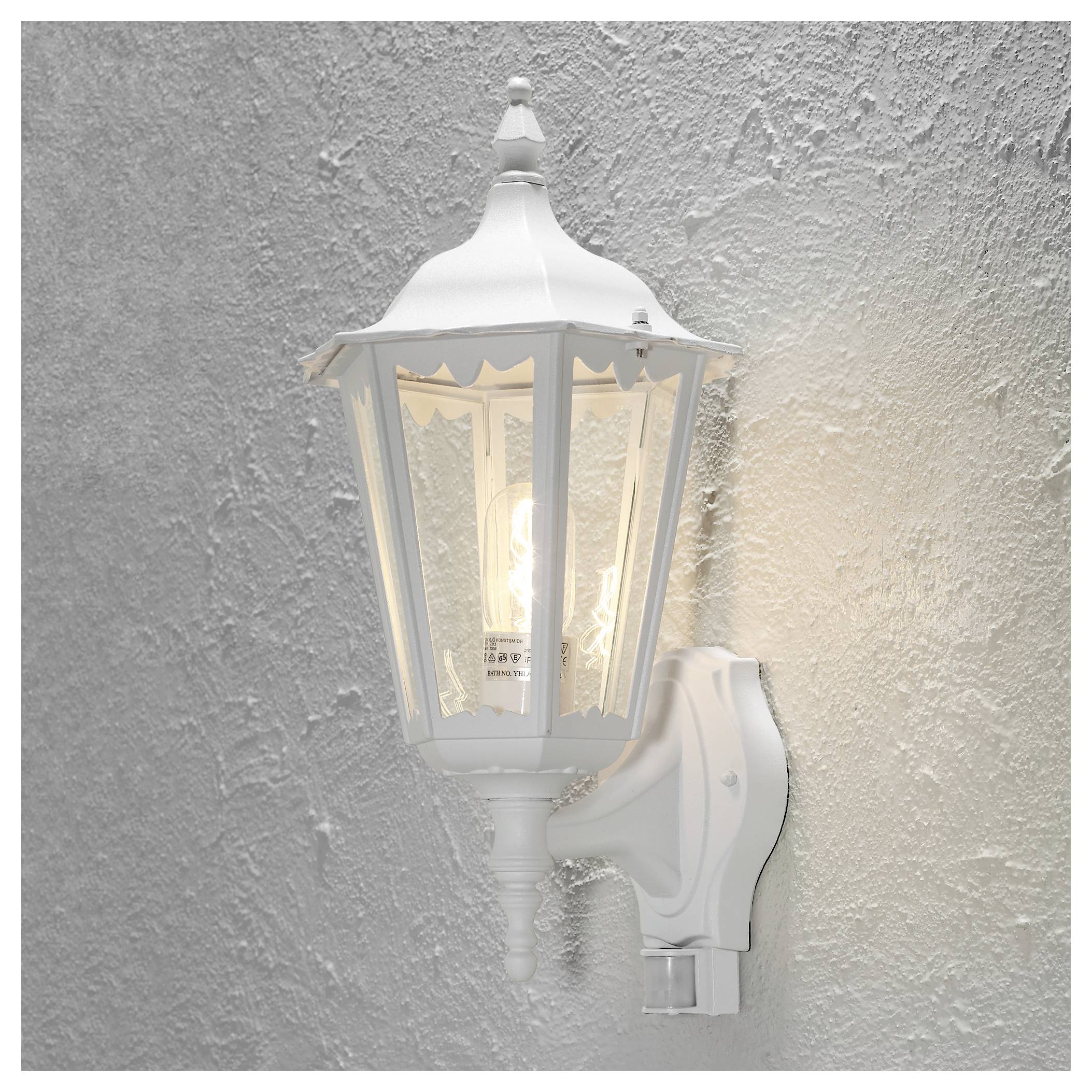 White wall-mounted outdoor lamp with classic lantern design, illuminated from the inside.
