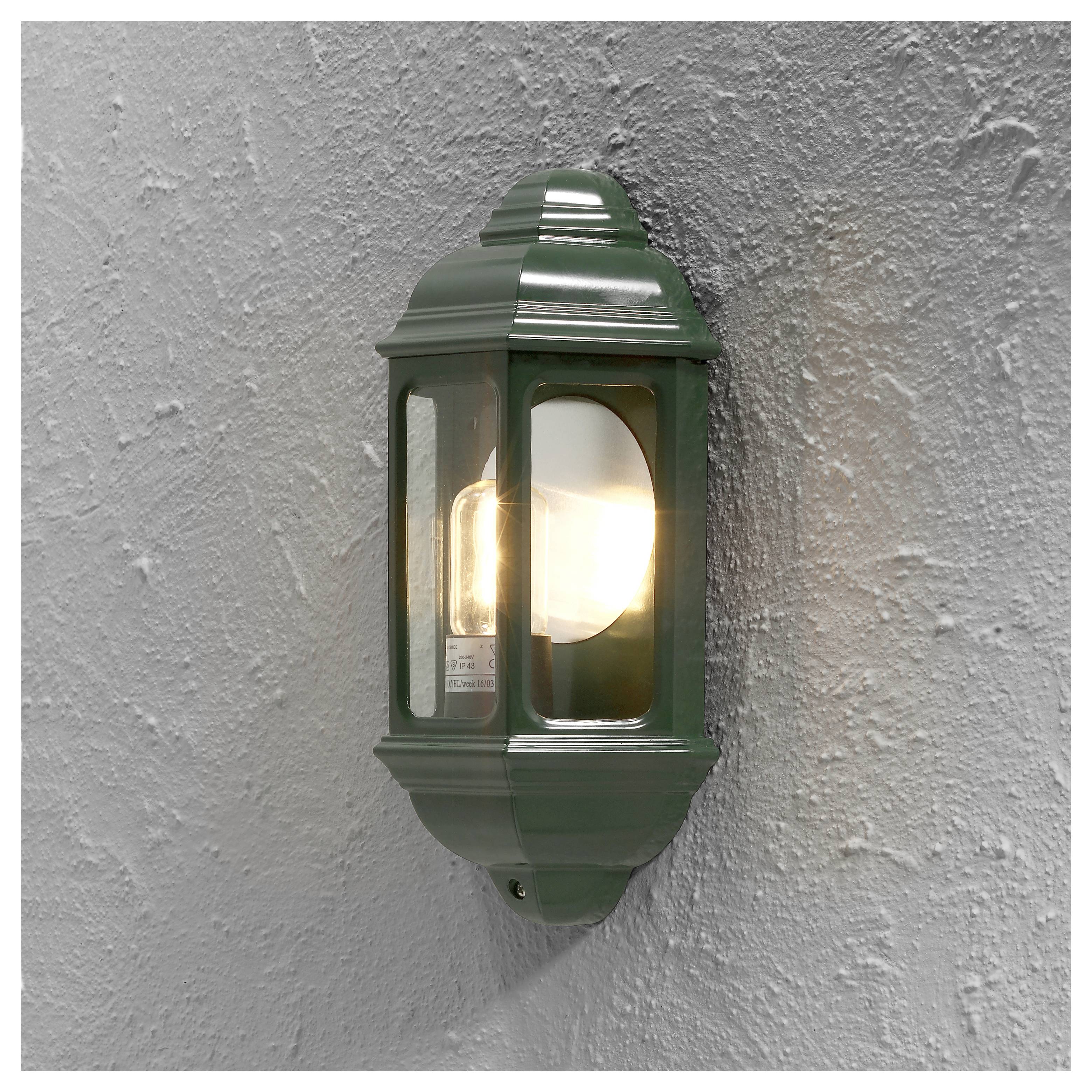 An outdoor wall-mounted lantern with a green frame illuminates a textured grey wall, providing ambient lighting.
