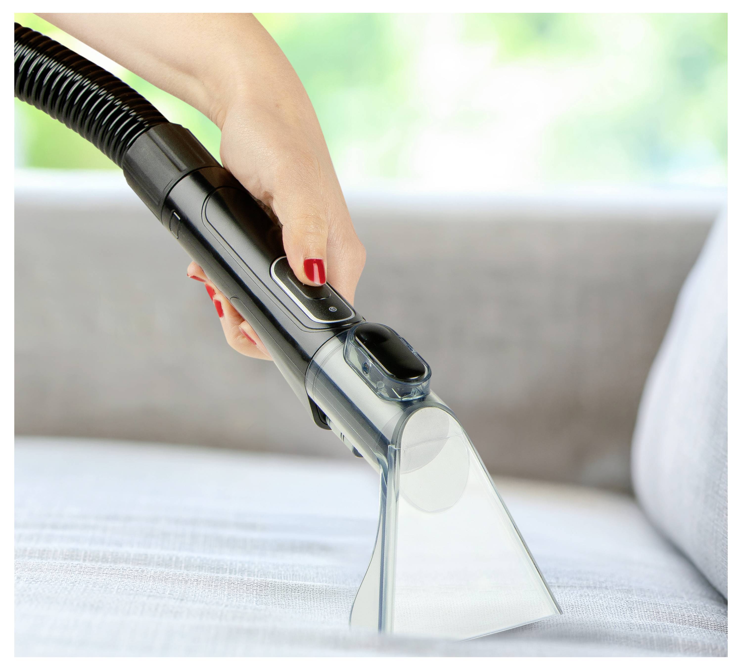 A hand using a vacuum cleaner attachment to clean a gray sofa, focusing on the upholstery.