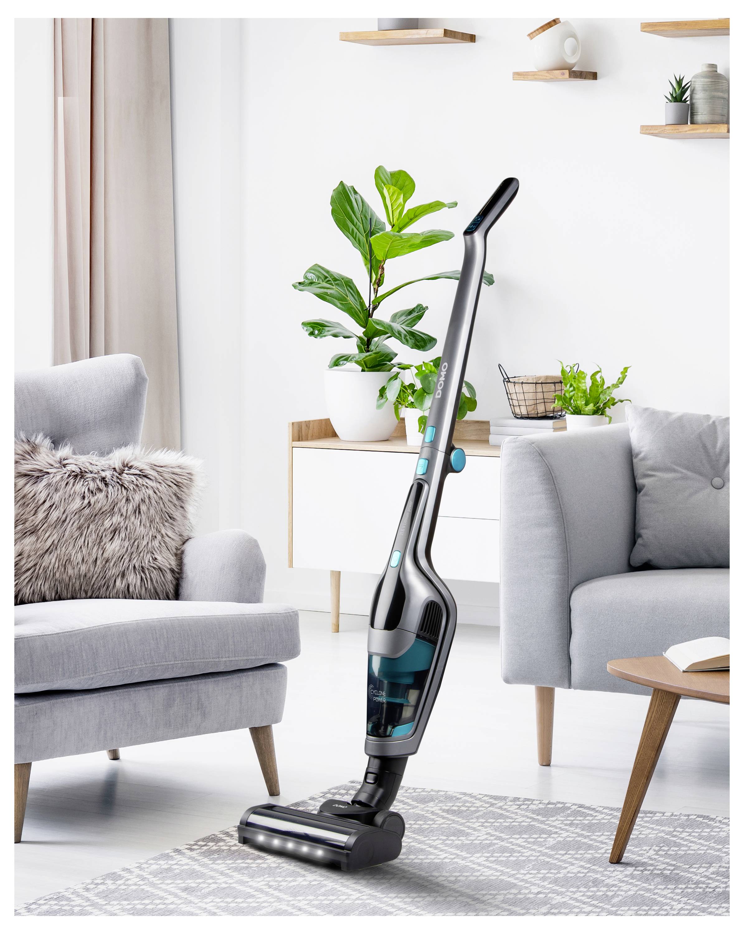 A modern, sleek vacuum cleaner stands upright in a stylish living room with contemporary furniture and green indoor plants.