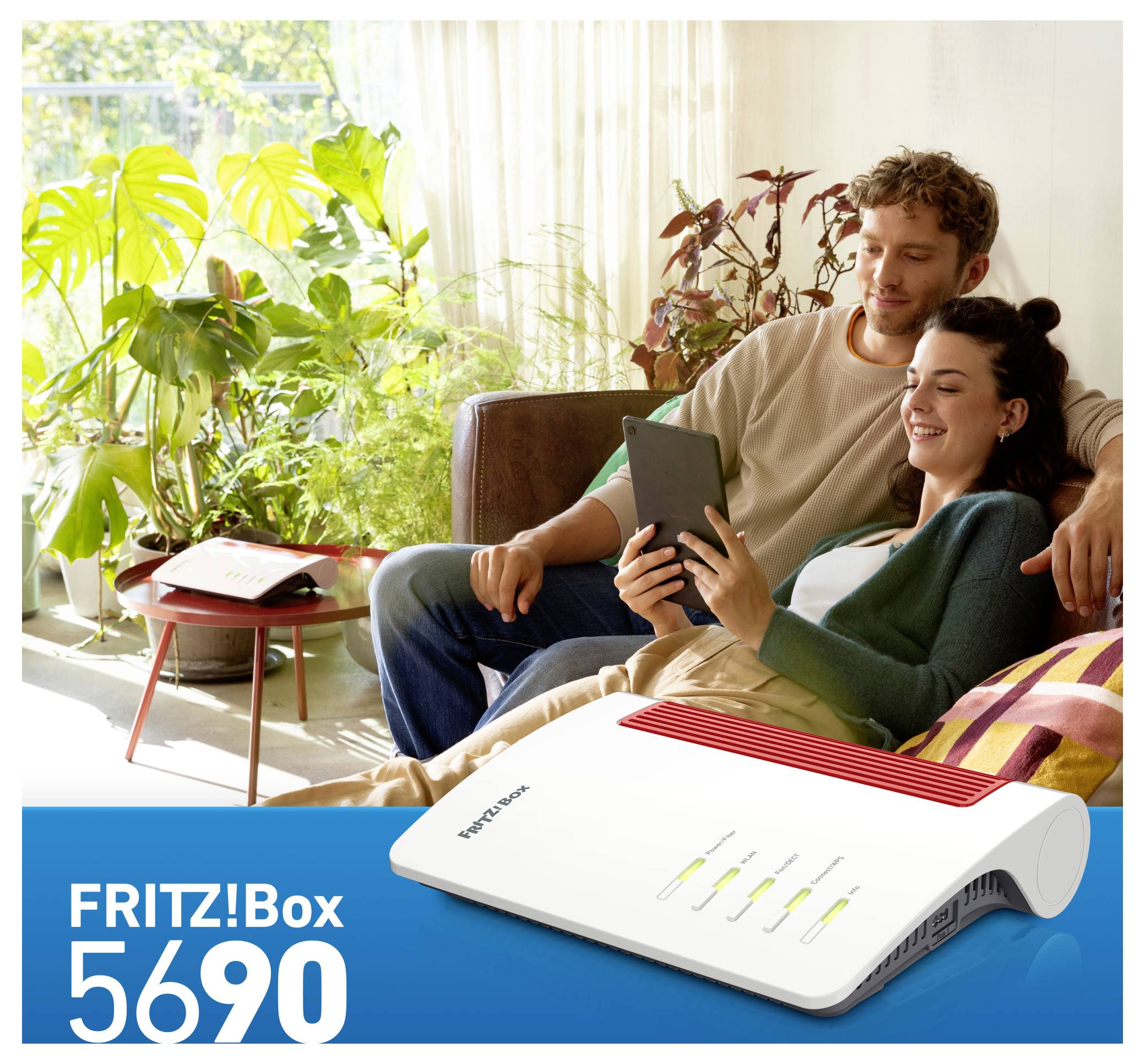 A smiling couple sits on a sofa, looking at a tablet. In the foreground, a FRITZ!Box 5690 router is shown with LED indicators lit.