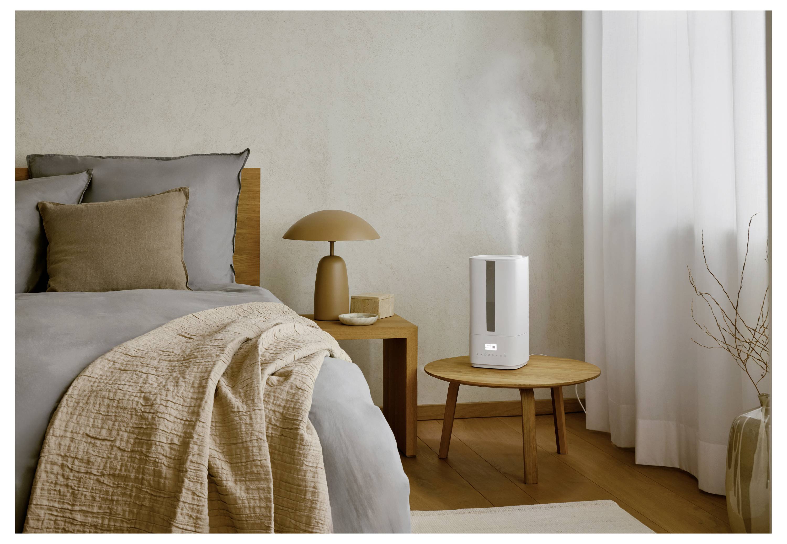 A cozy bedroom with neutral tones features a neatly made bed and a wooden side table holding a modern humidifier emitting mist.
