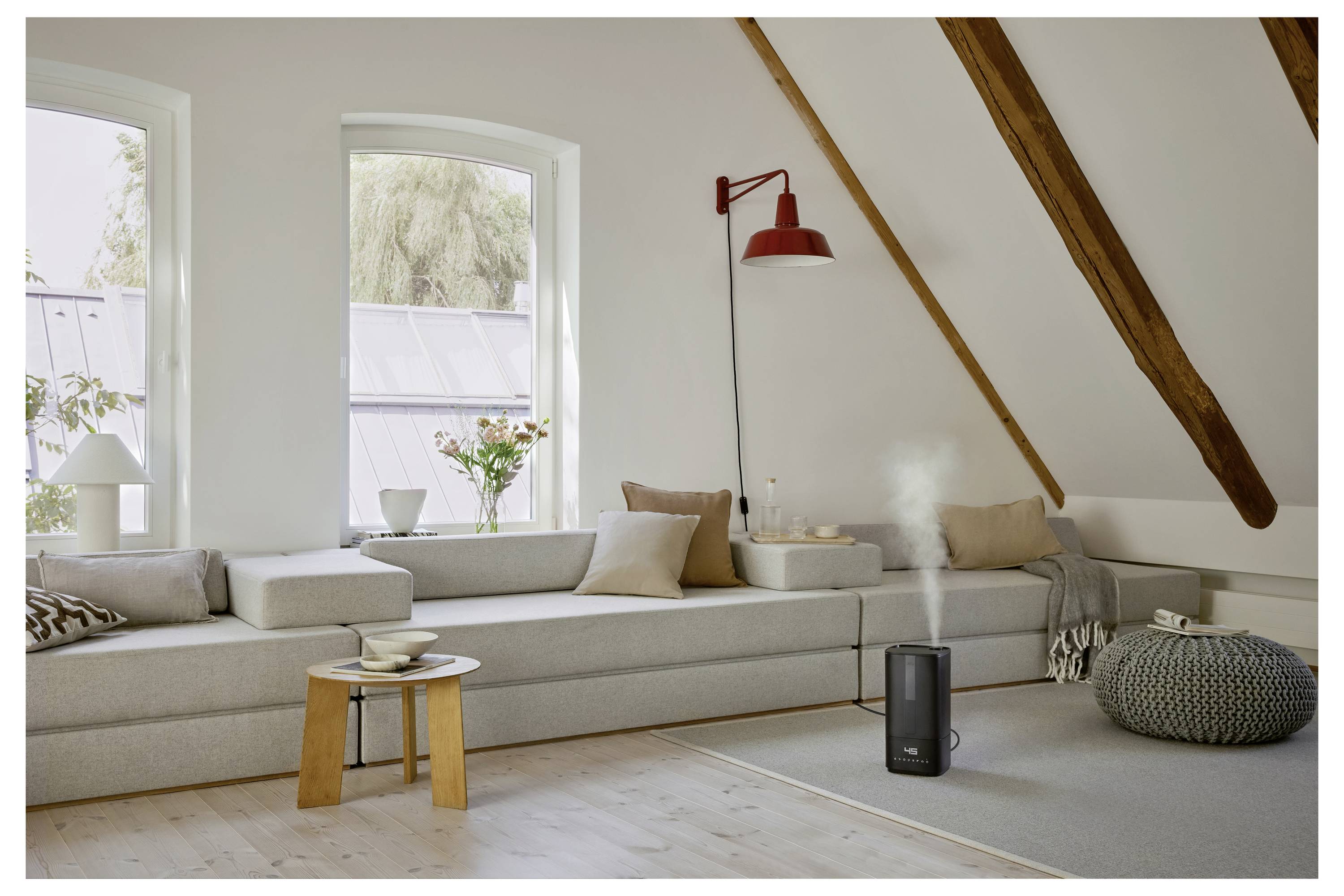 Spacious living room with a minimalist design, featuring a light gray sectional sofa, red wall lamp, and a black humidifier emitting steam.