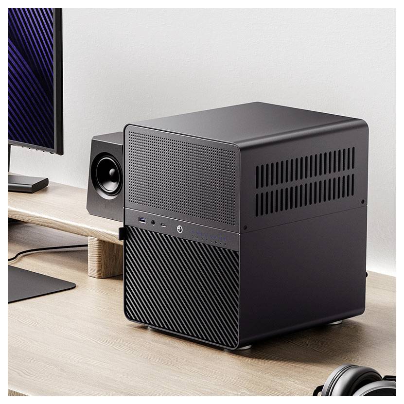 A sleek, black desktop computer on a wooden desk next to a monitor and speaker, suggesting a modern office or home workspace setup.