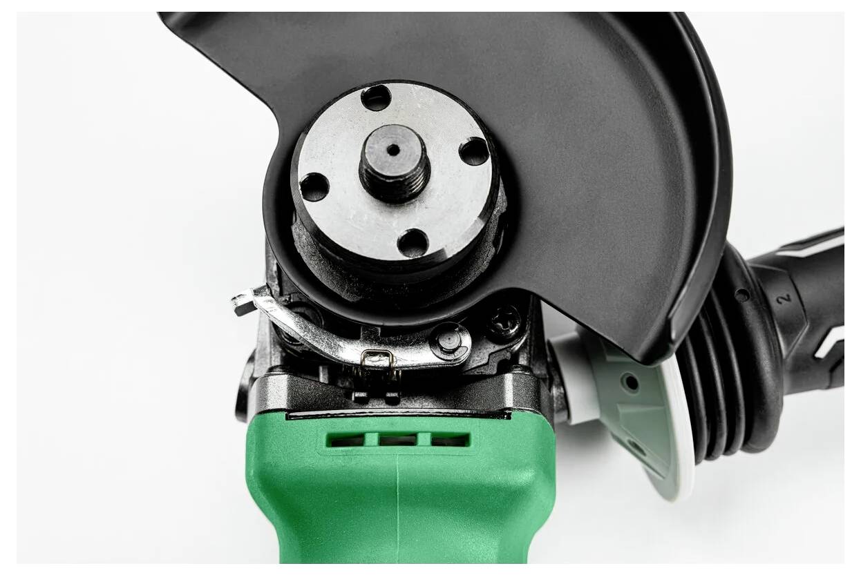 Close-up of a power angle grinder with a green handle, black guard, and spindle head.