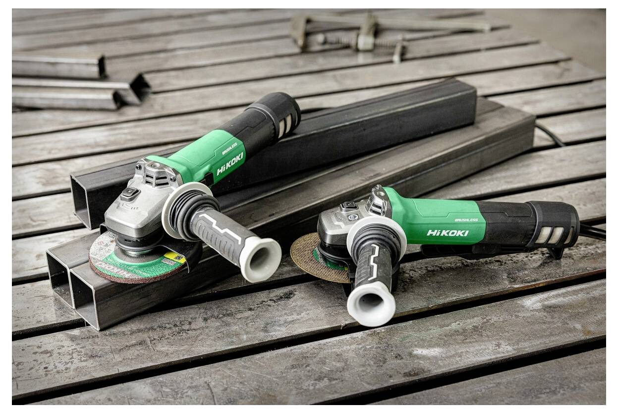 Two green and gray angle grinders branded 'Hikoki' resting on metal beams on a wooden surface, suggesting construction or metalwork.