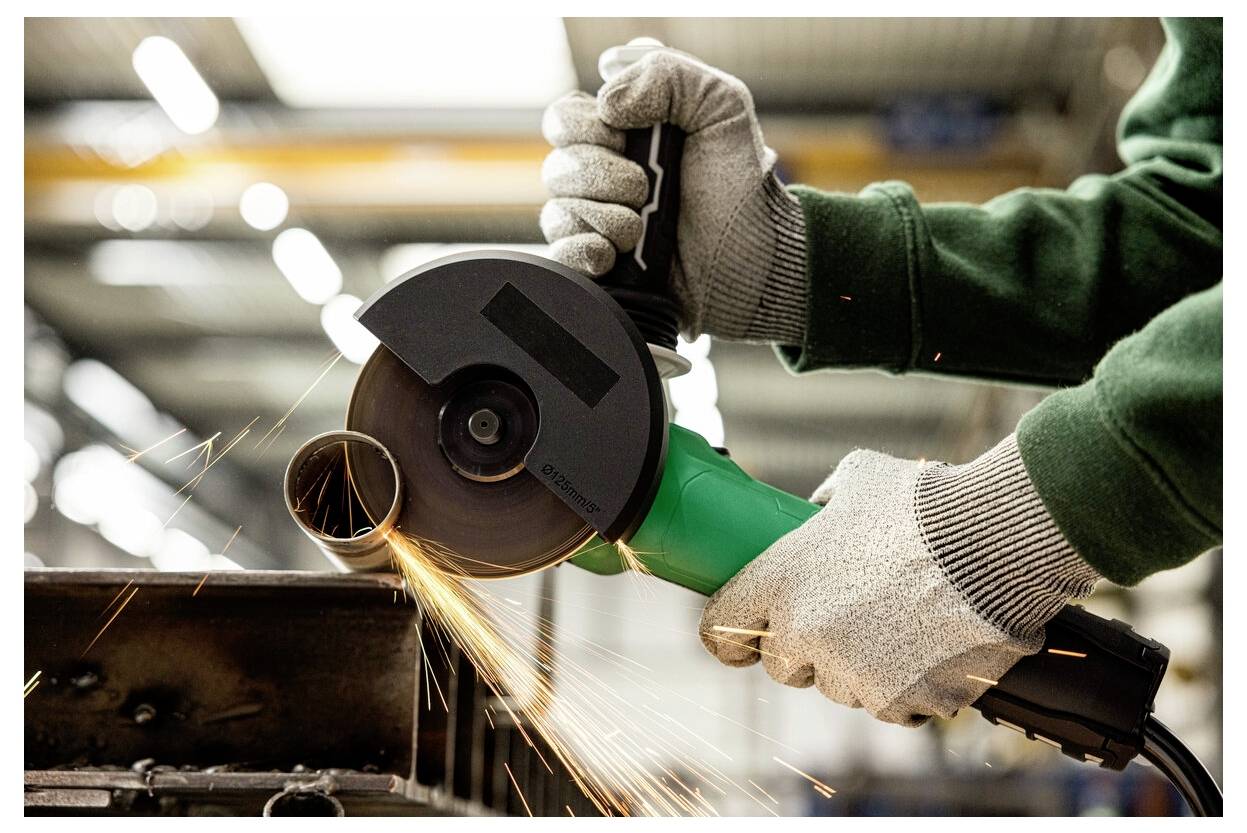 Person using an angle grinder, creating sparks while cutting a metal pipe in a workshop. Gloves and safety gear are visible.