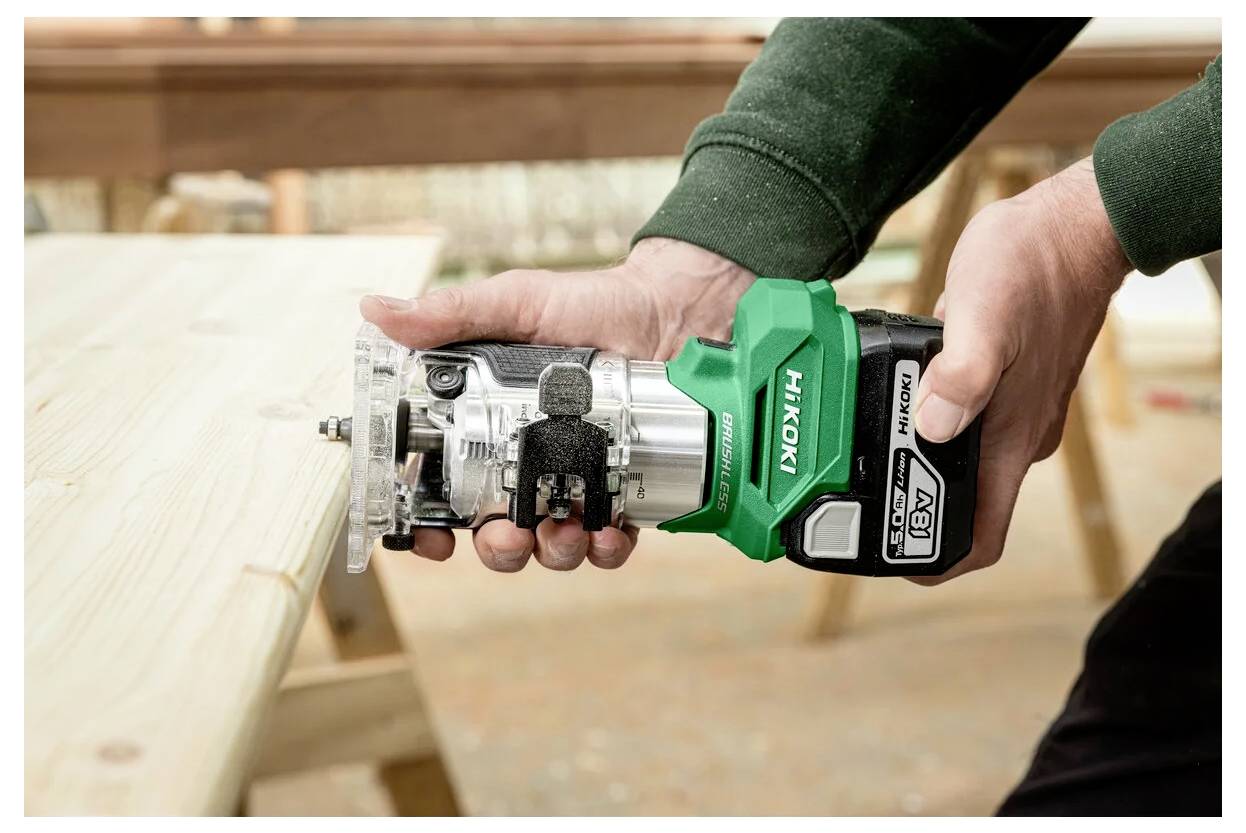 A person uses a Hikoki power tool to work on a wooden plank, focusing on precision and craftsmanship in a workshop setting.