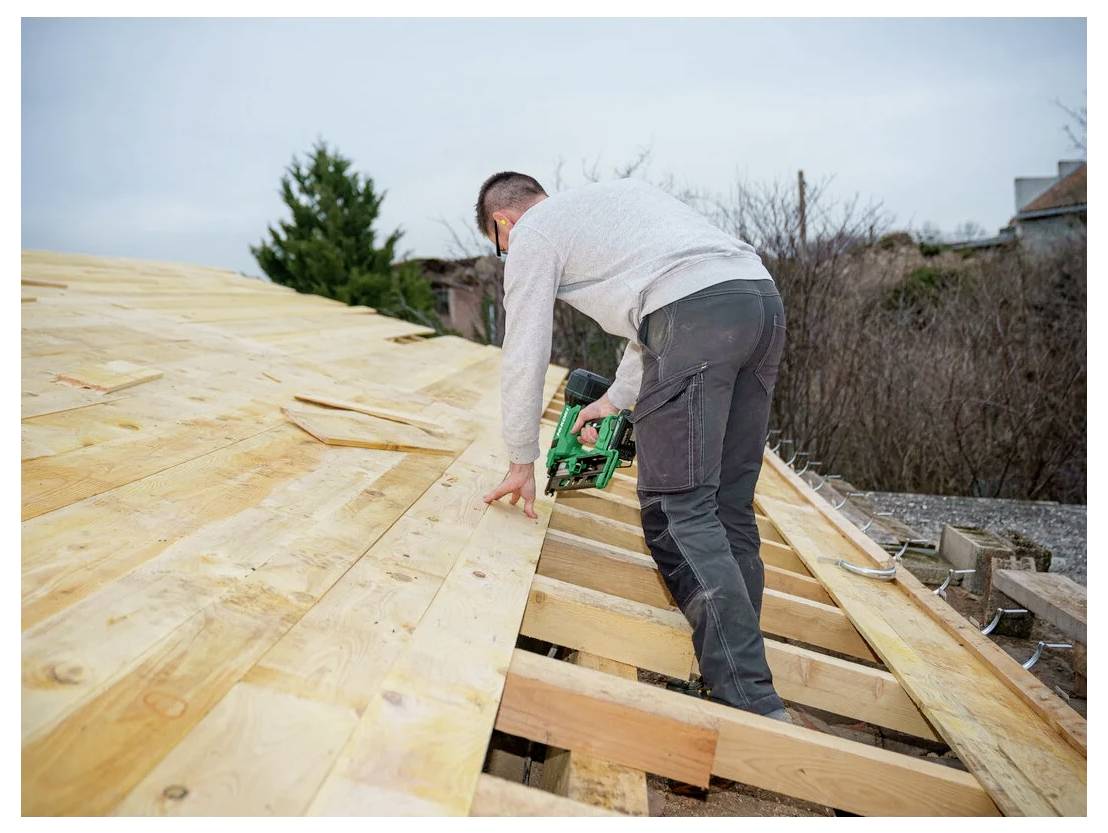 A person is using a power tool to install wooden boards on a roof, focusing on aligning and securing each piece.