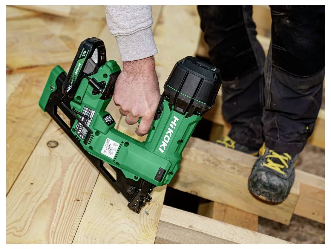 A person using a green nail gun to fasten wooden planks during a construction project.