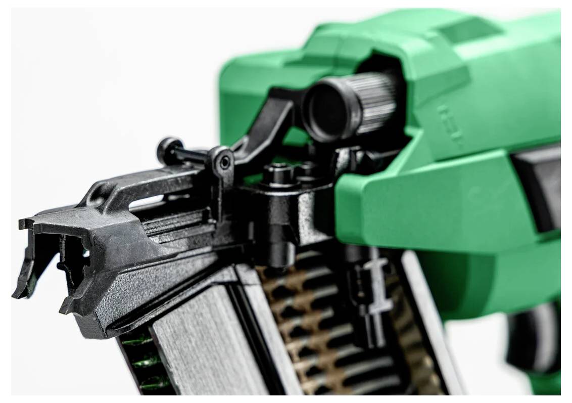 Close-up of a green and black pneumatic nail gun, showing the trigger and nail loading mechanism.