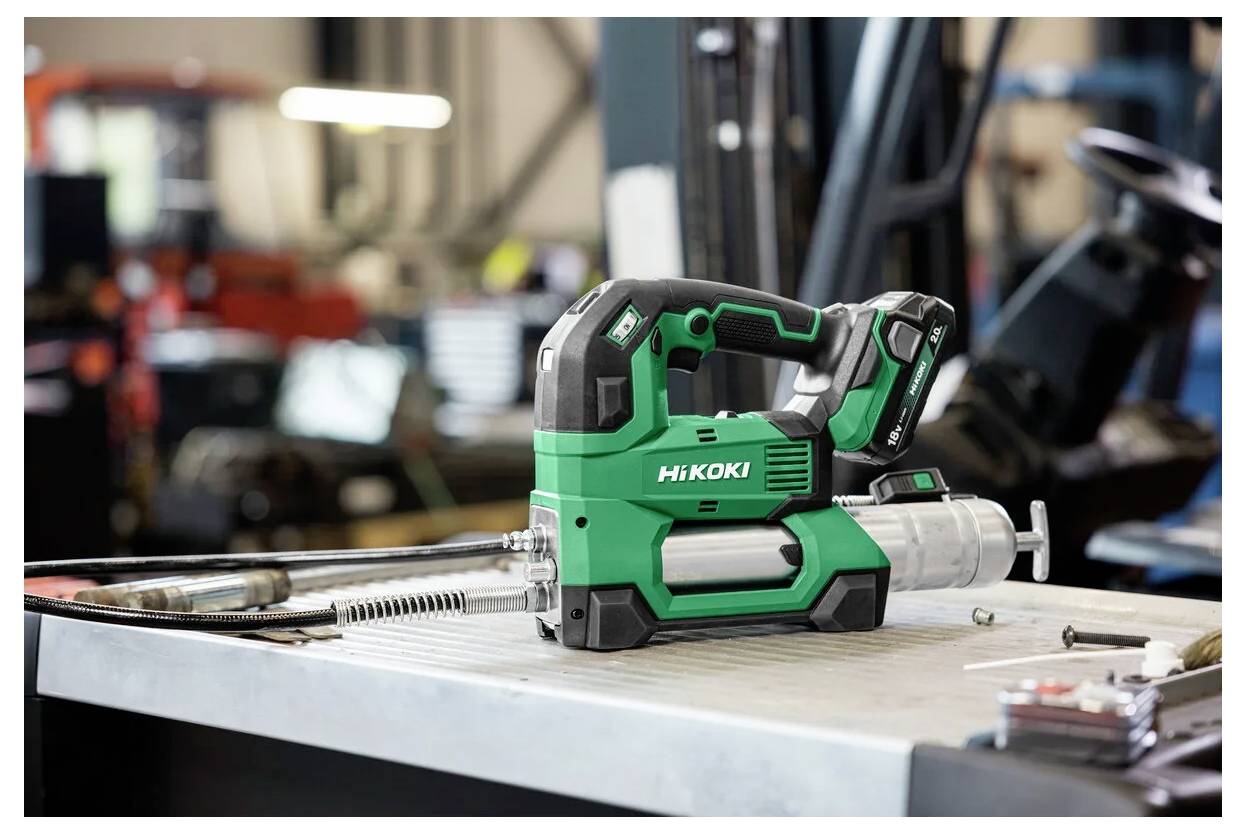 A green HiKoki power tool with a nozzle sits on a workbench in a workshop, surrounded by various tools and machinery.