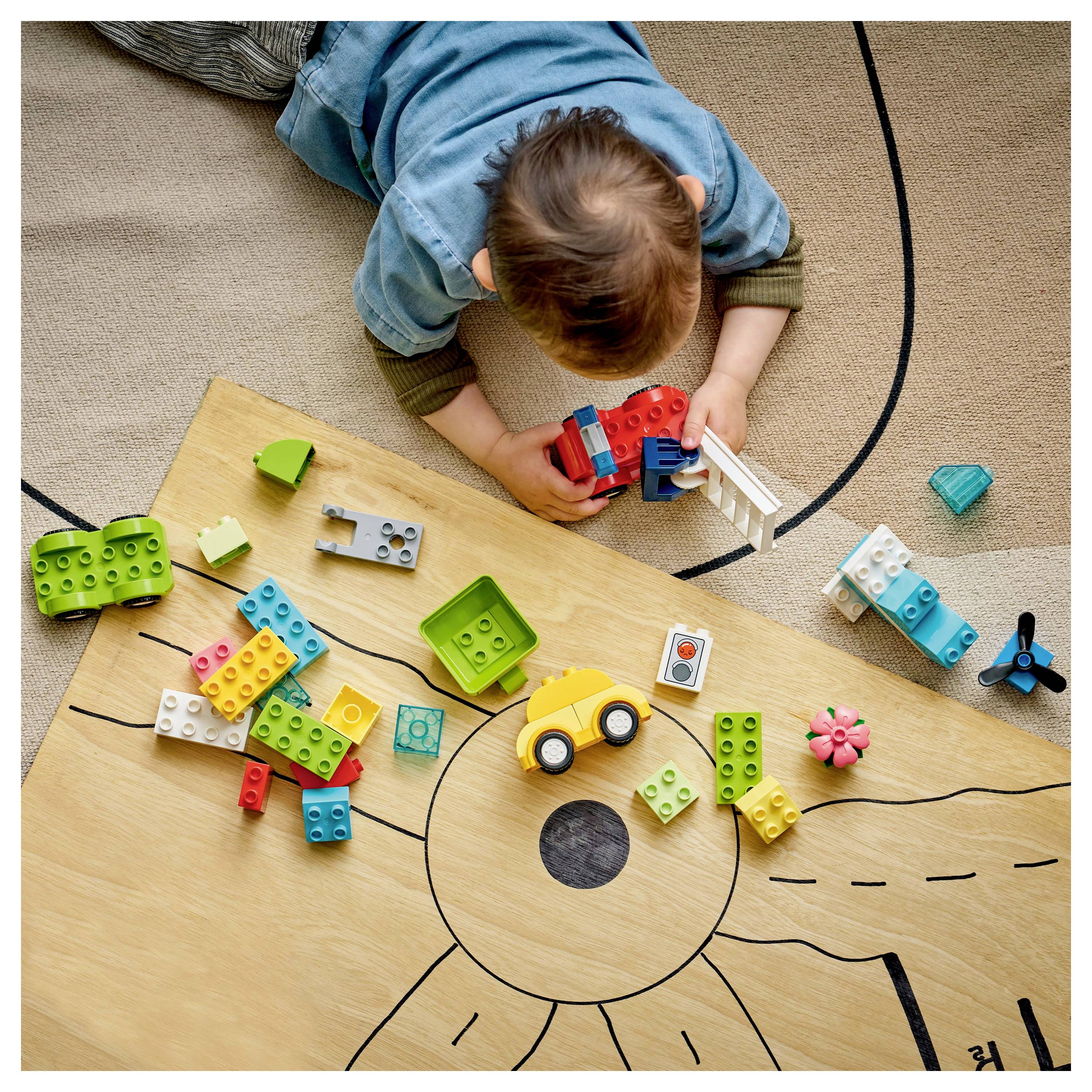 Child playing with colorful toy blocks on a play mat, featuring a yellow toy car and various shaped pieces scattered around.