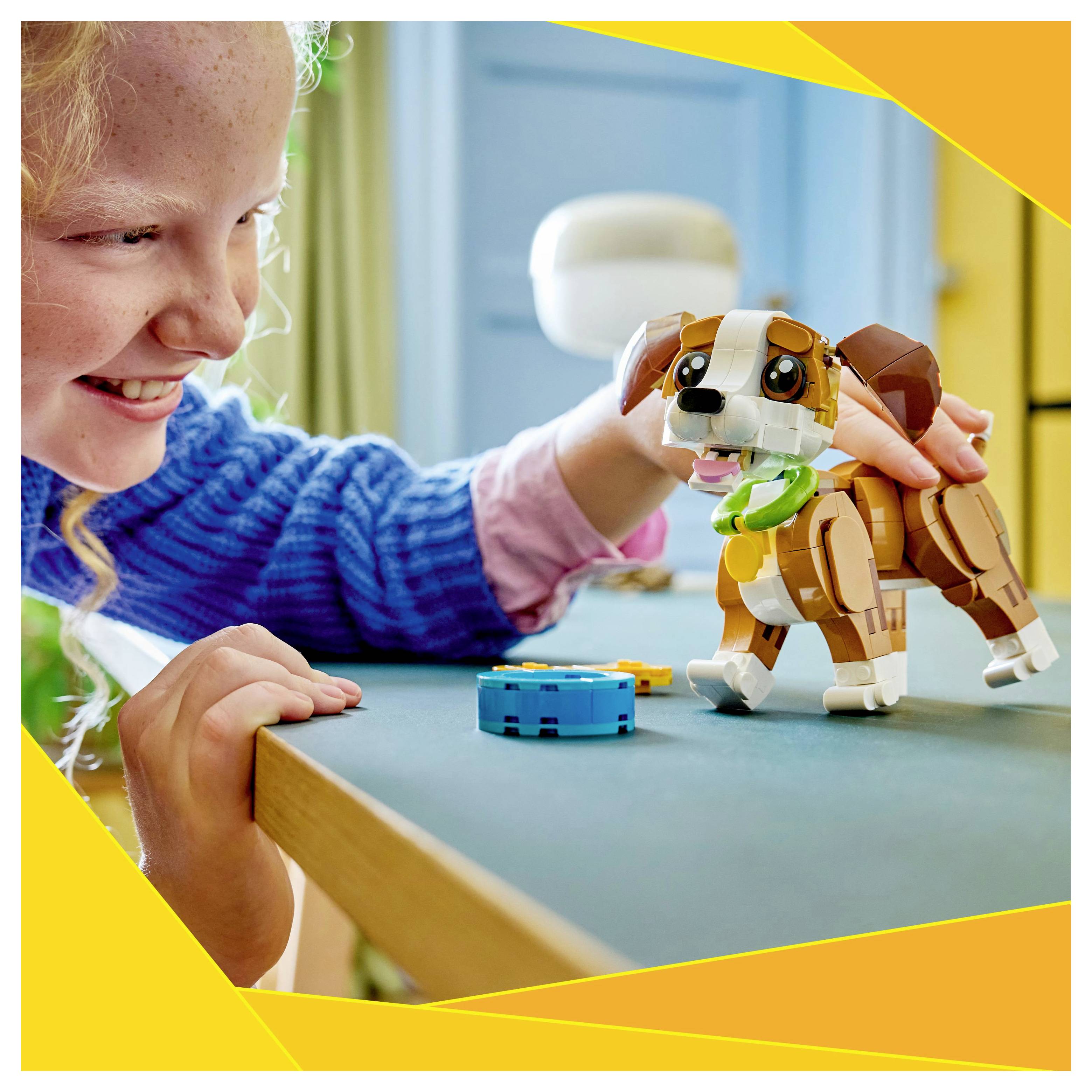 A child in a blue sweater happily plays with a toy dog on a table. The background is colorful and blurred.