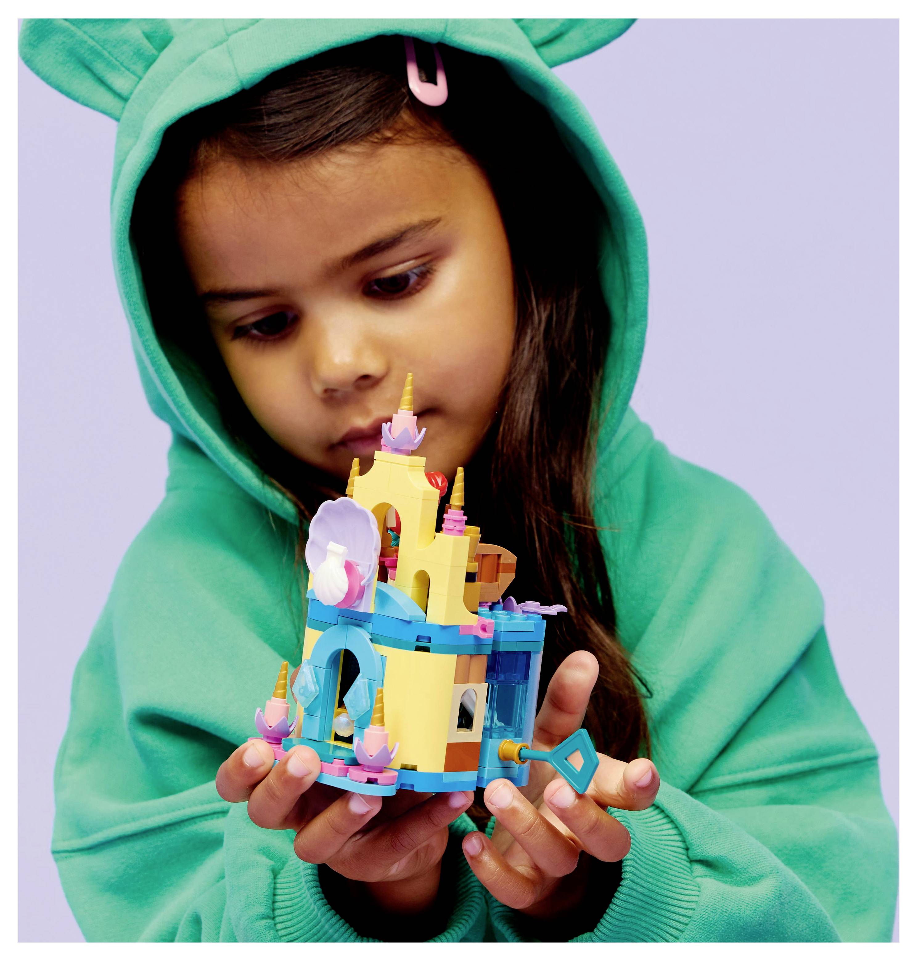 A child in a green hoodie carefully examines a colorful LEGO castle model, focusing intently on its details.