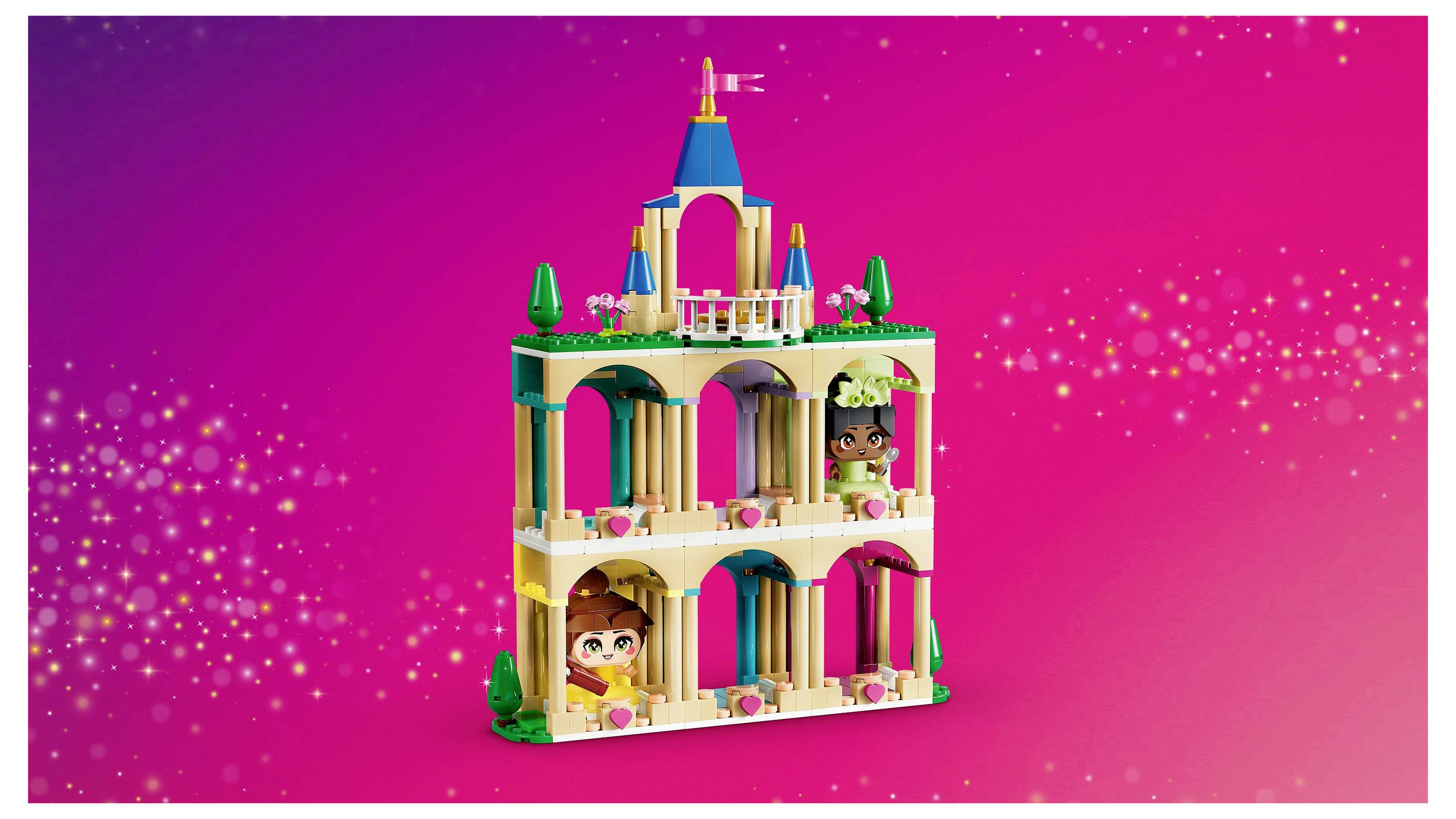 A colorful toy building with arches and towers stands against a bright pink background, featuring two smiling figurines on different levels.