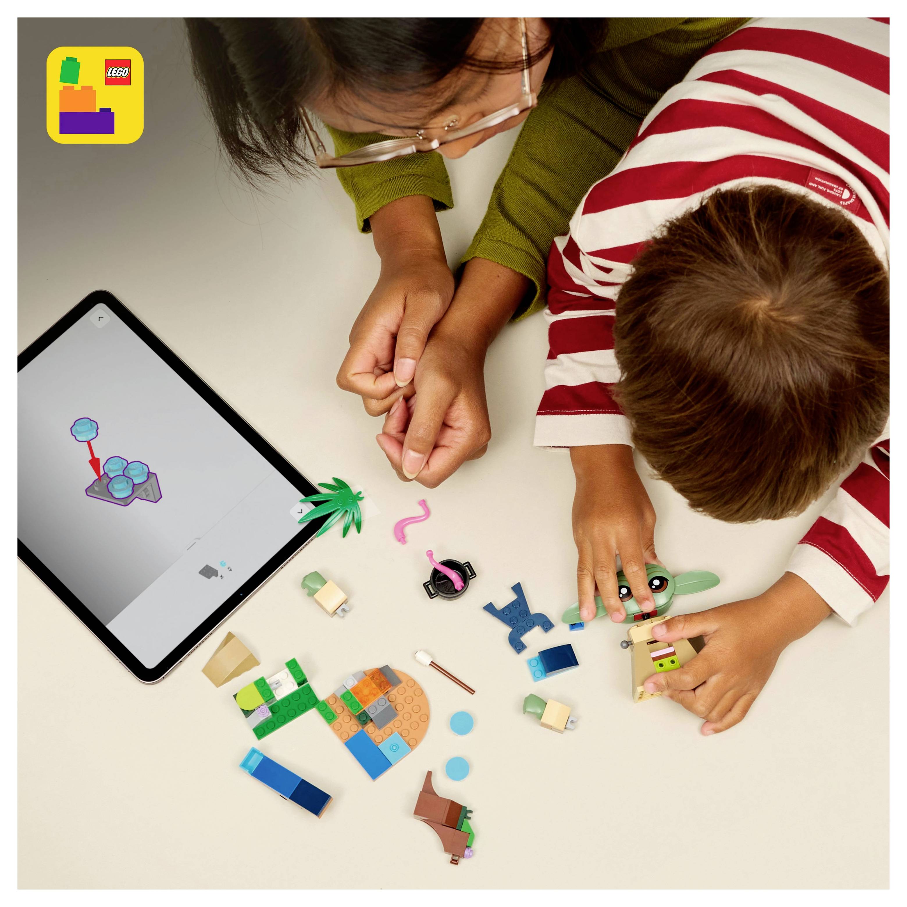 A child and an adult play with LEGO bricks on a table next to a tablet displaying a LEGO model. The LEGO logo is in the top left corner.