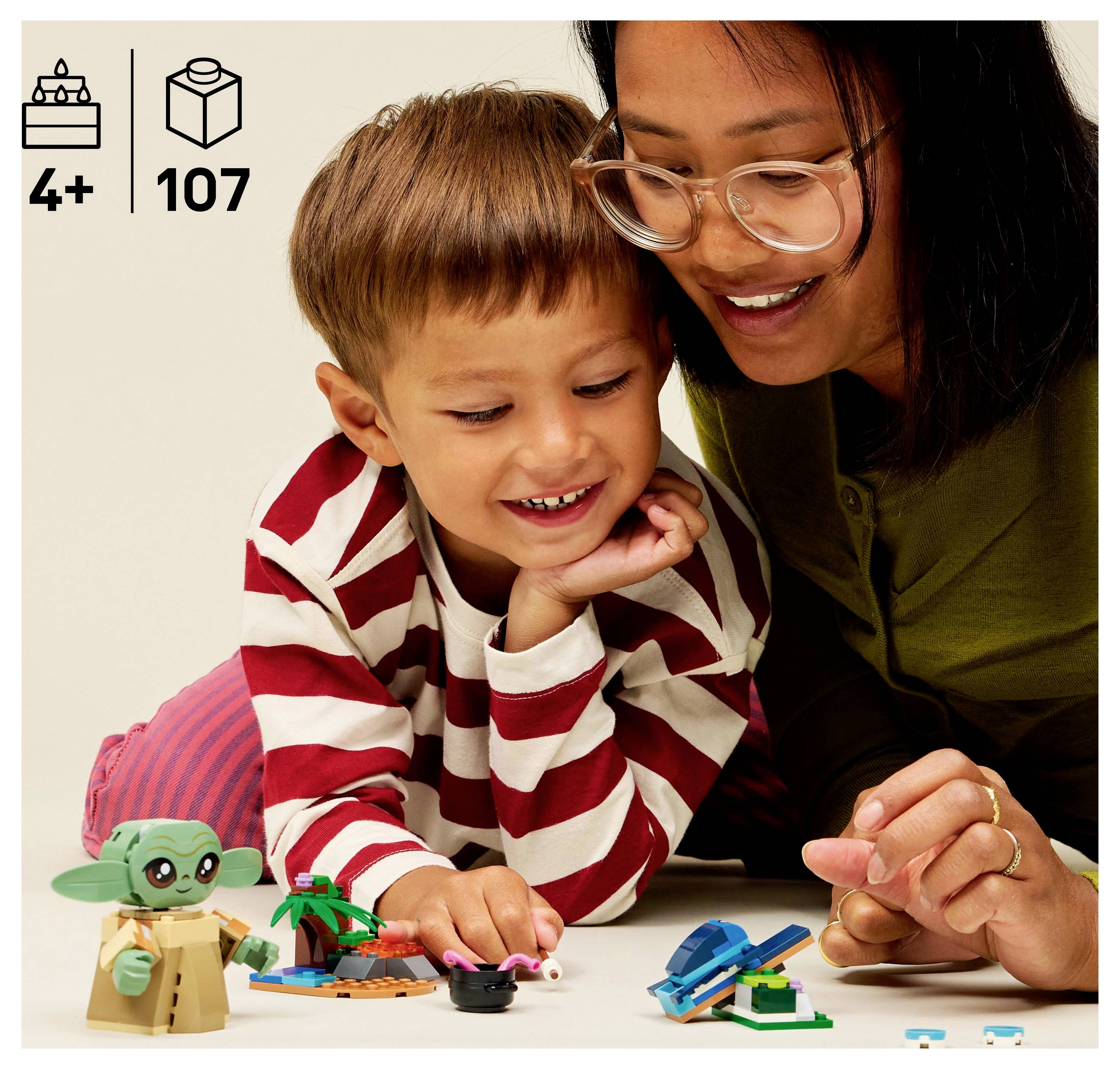 A woman and a child play with small toy figures on a white surface. The child wears a striped shirt, and the woman wears glasses.