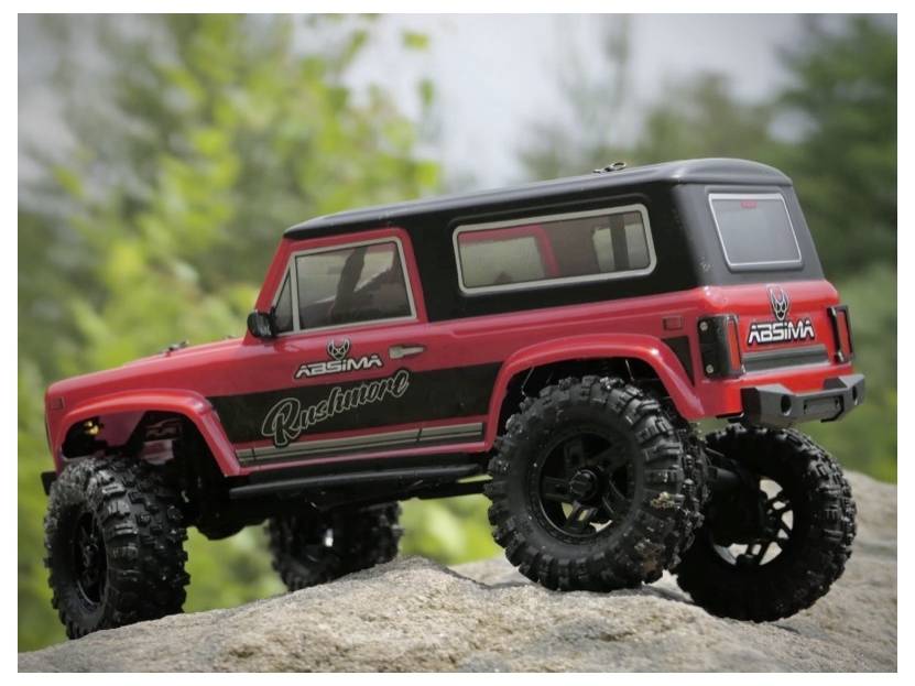 A red remote control off-road vehicle with large tires is shown on a rock, set against a blurred natural background.