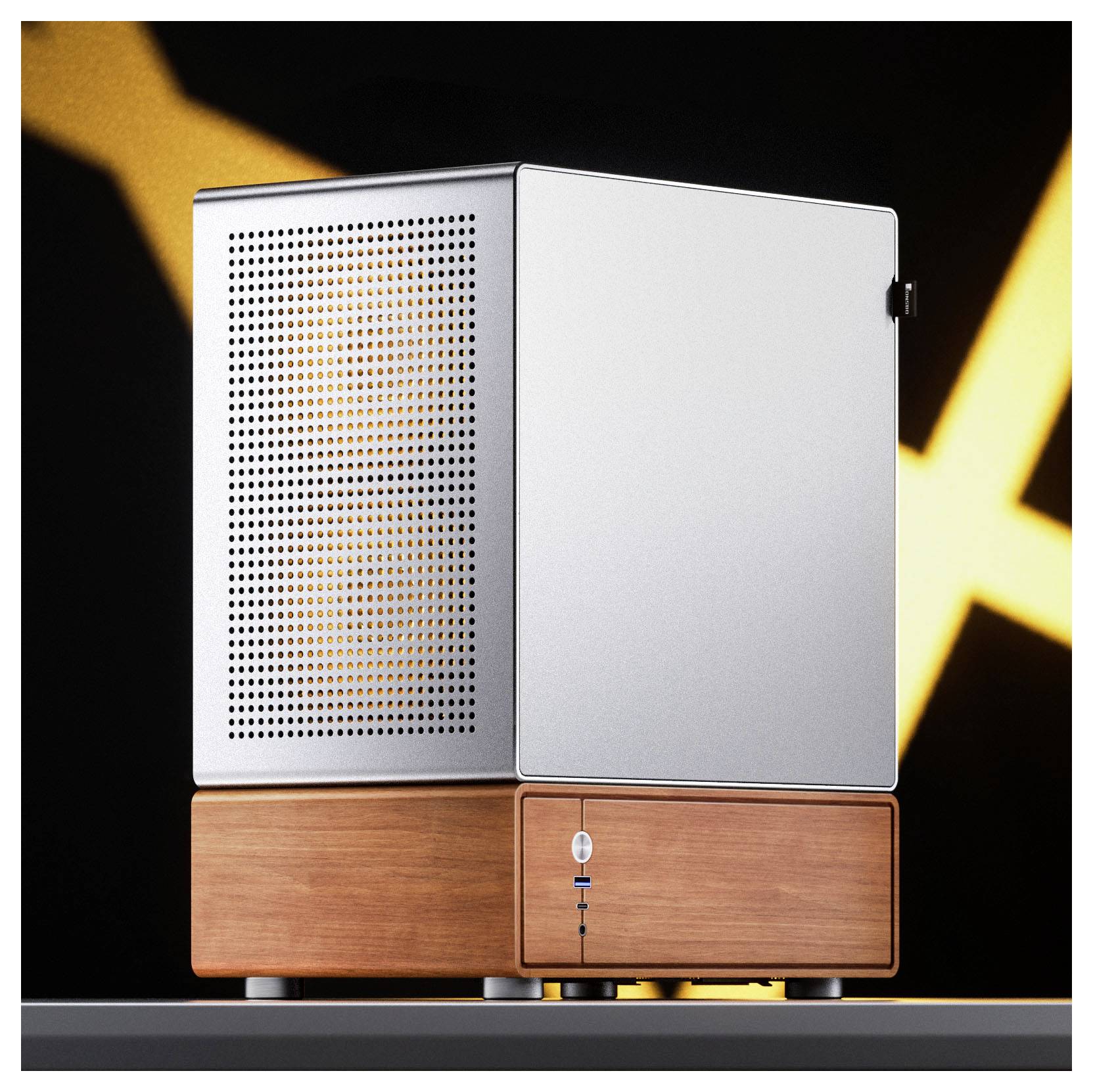 A small, modern desktop computer with a sleek metal finish and a wooden base sits on a gray surface against a blurred black and yellow background.