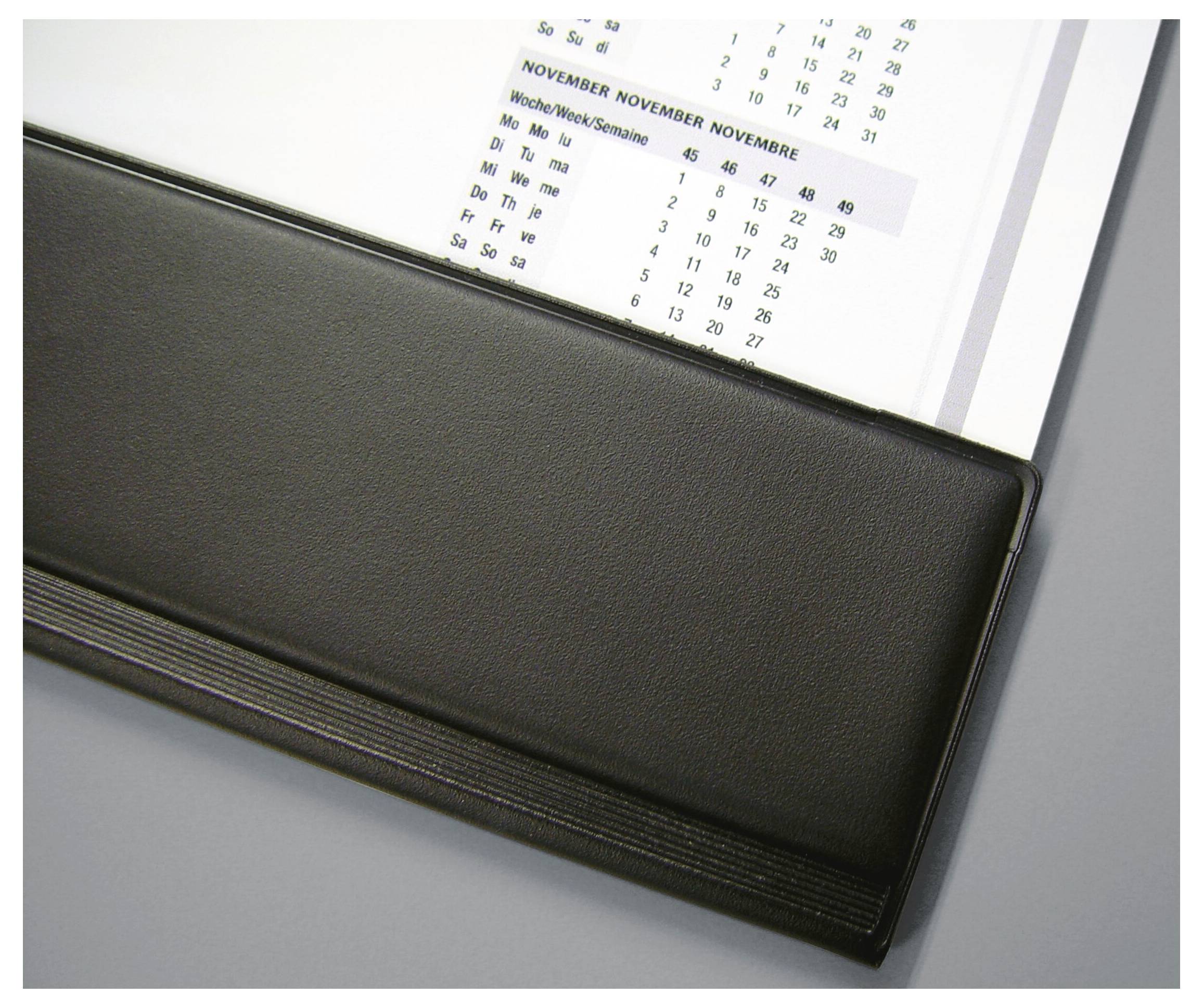 A black desk pad with a visible partial calendar, showing the month of November and weekdays, placed on a gray surface.