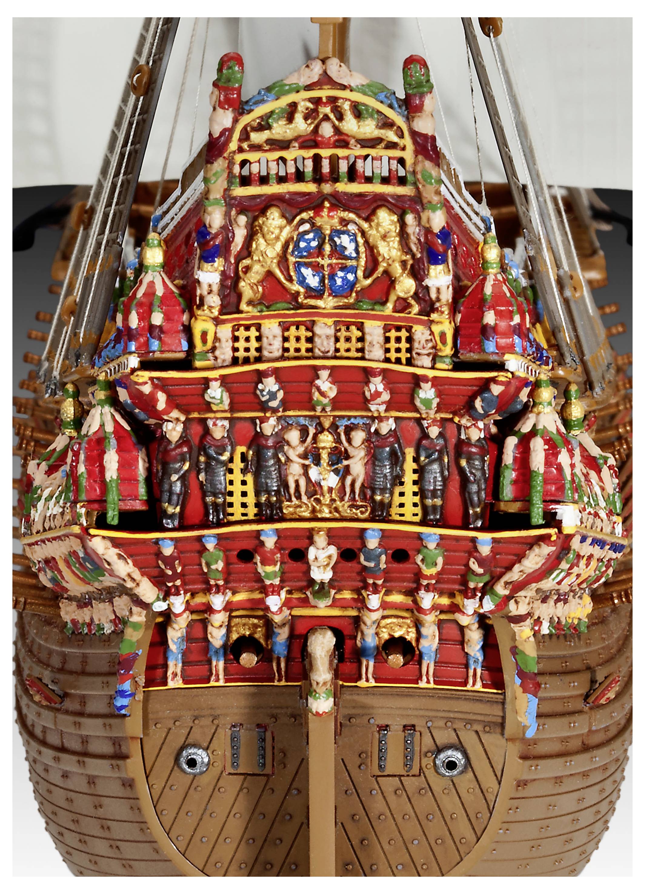 The image depicts an ornately decorated wooden ship's stern with intricate carvings and colorful painted figures, featuring sailors and symbols.