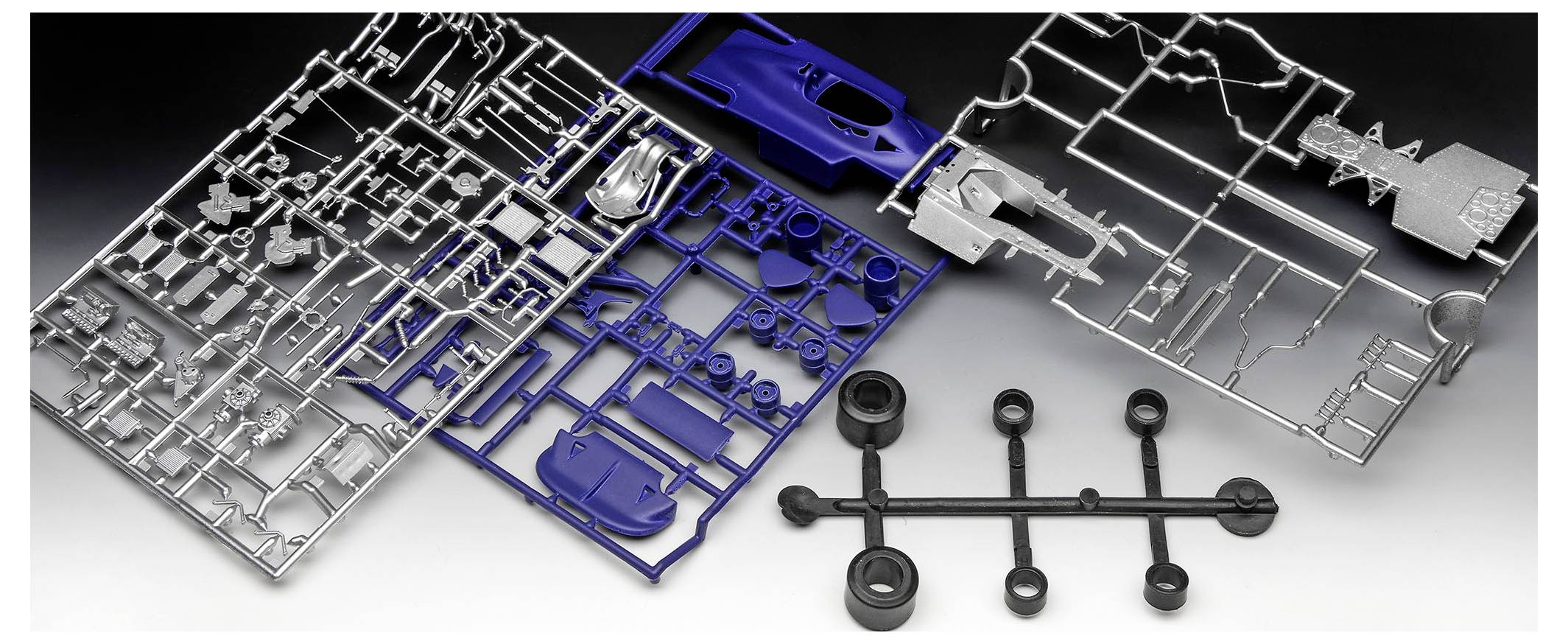 Plastic model kit parts on sprues, including blue, black, and gray pieces for assembling a model vehicle, laid out on a surface.