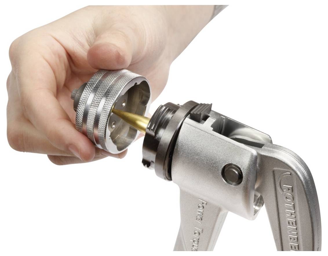 A person is inserting a brass fitting into a silver metal tool. The tool has a textured handle and appears to be used for pressing or crimping.